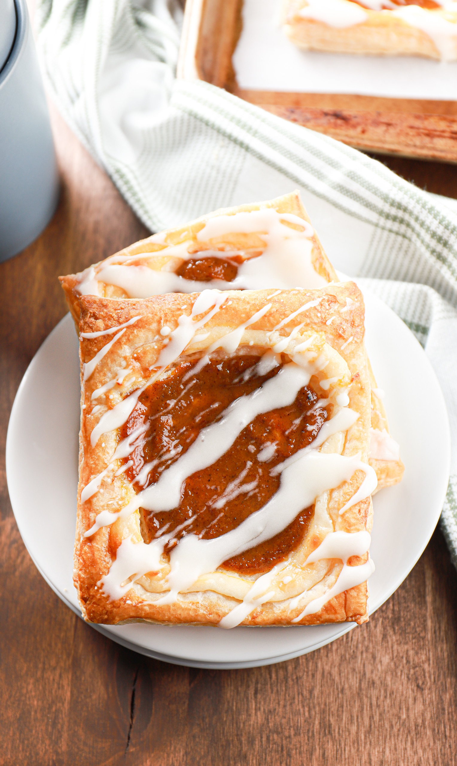 Two pumpkin cream cheese danishes on a small white plate with the remaining batch of the danishes in the background.