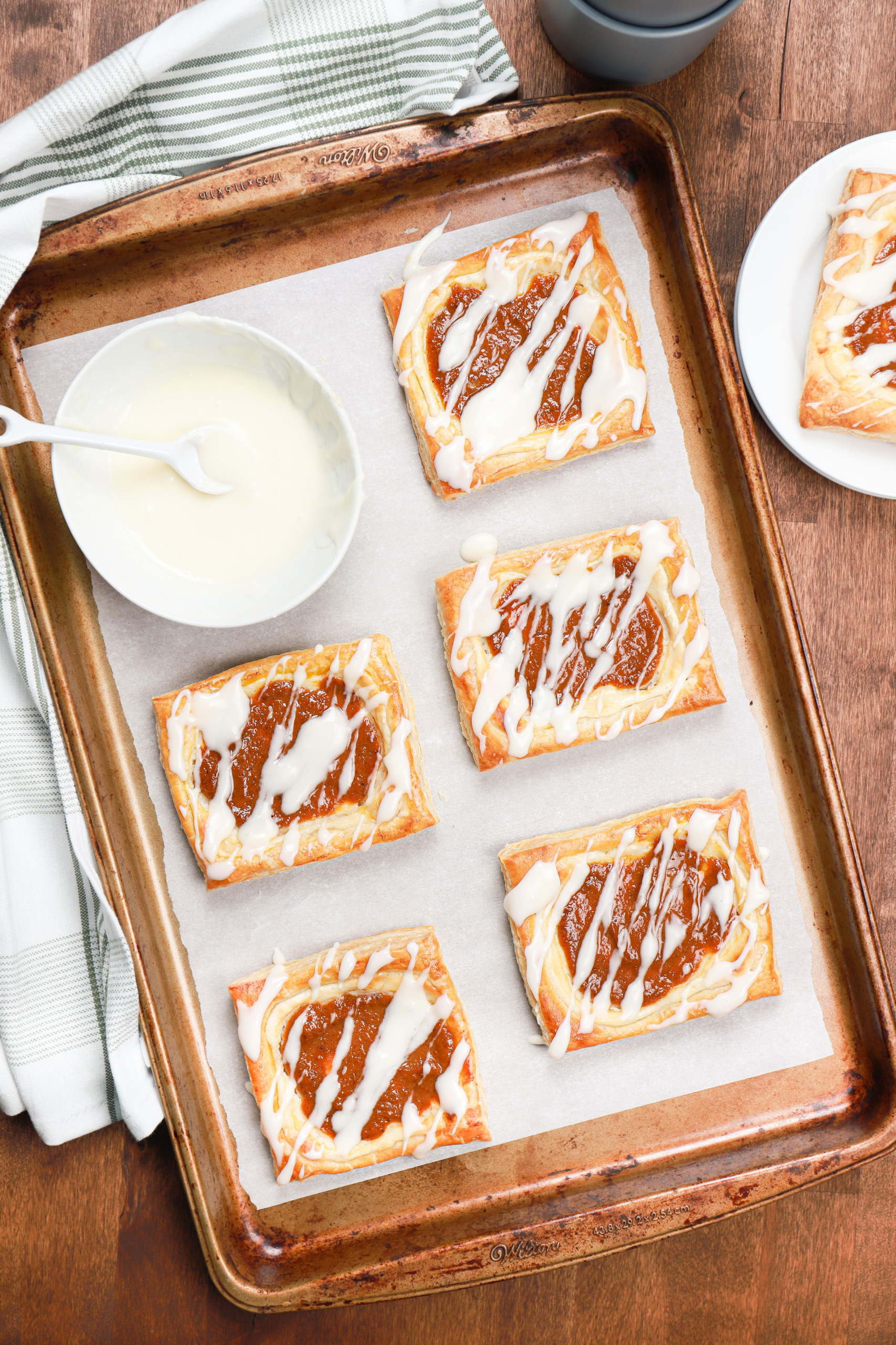 Overhead view of a batch of pumpkin cream cheese danishes drizzled with glaze on a parchment paper lined baking sheet.