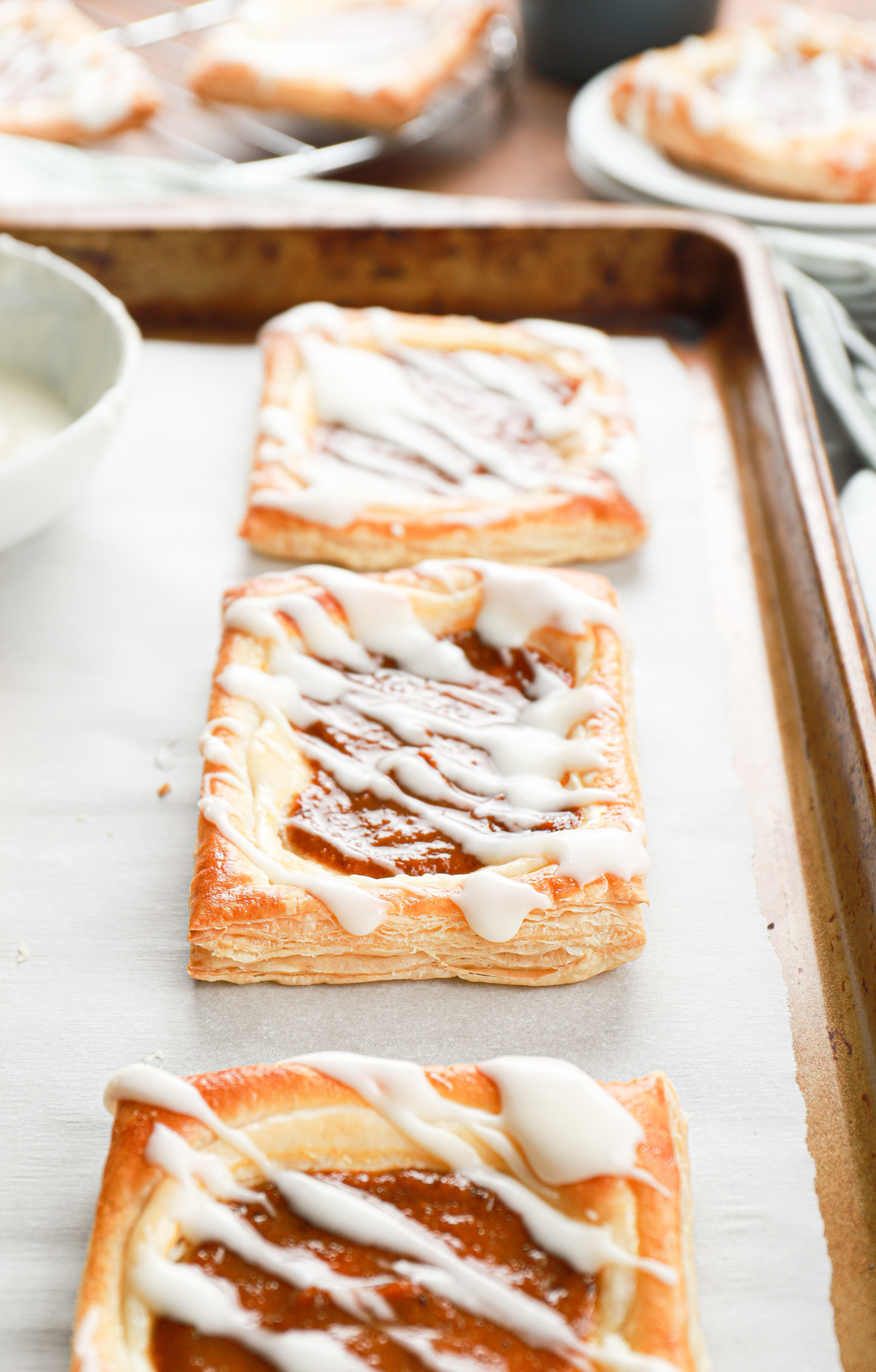 Side view of a pumpkin cream cheese danish on a parchment paper lined baking sheet.