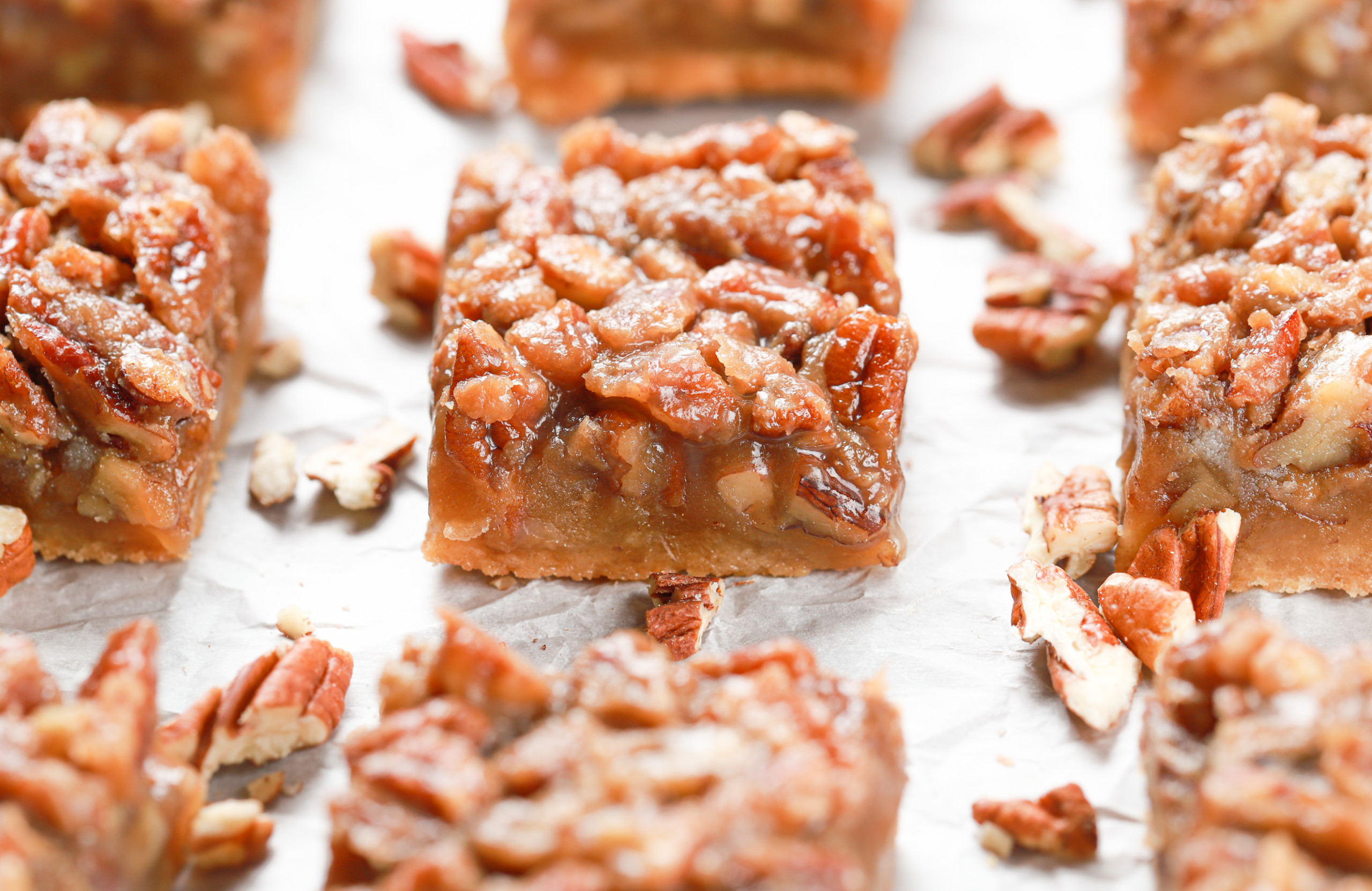 Side view of a maple pecan pie bar on a piece of parchment paper surrounded by more bars.