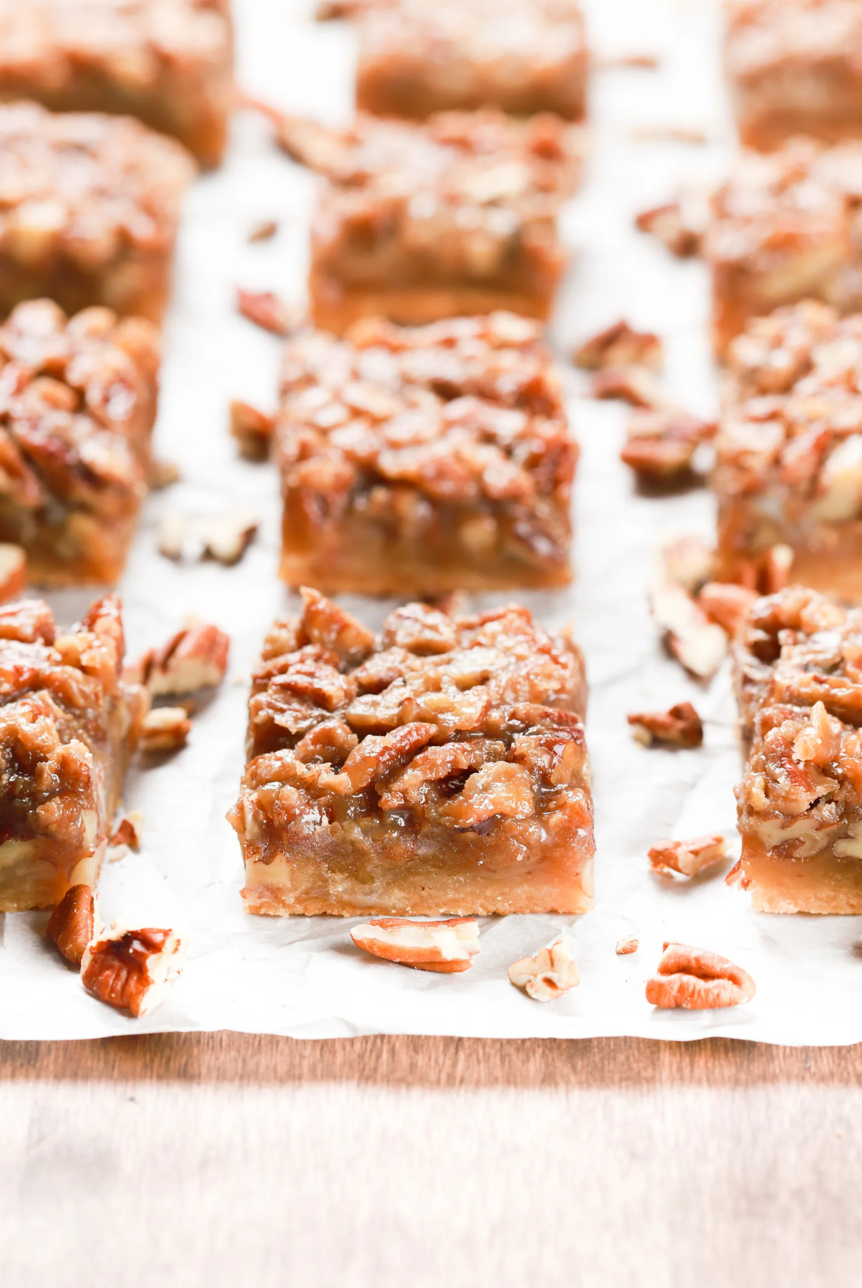 A side view of a batch of maple pecan pie bars on a piece of parchment paper.