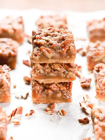 Stack of three maple pecan pie bars on a piece of parchment paper with more bars surrounding the stack.