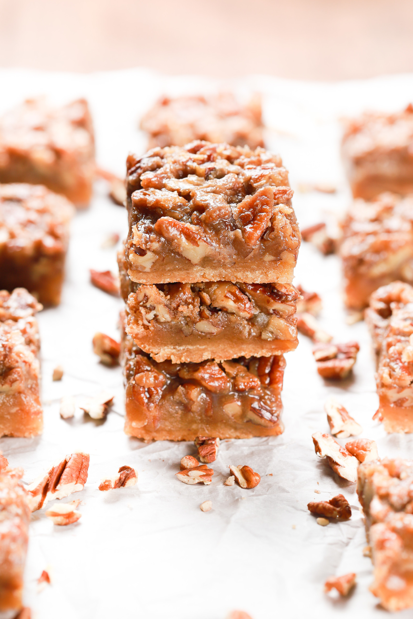 Stack of three maple pecan pie bars on a piece of parchment paper with more bars surrounding the stack.