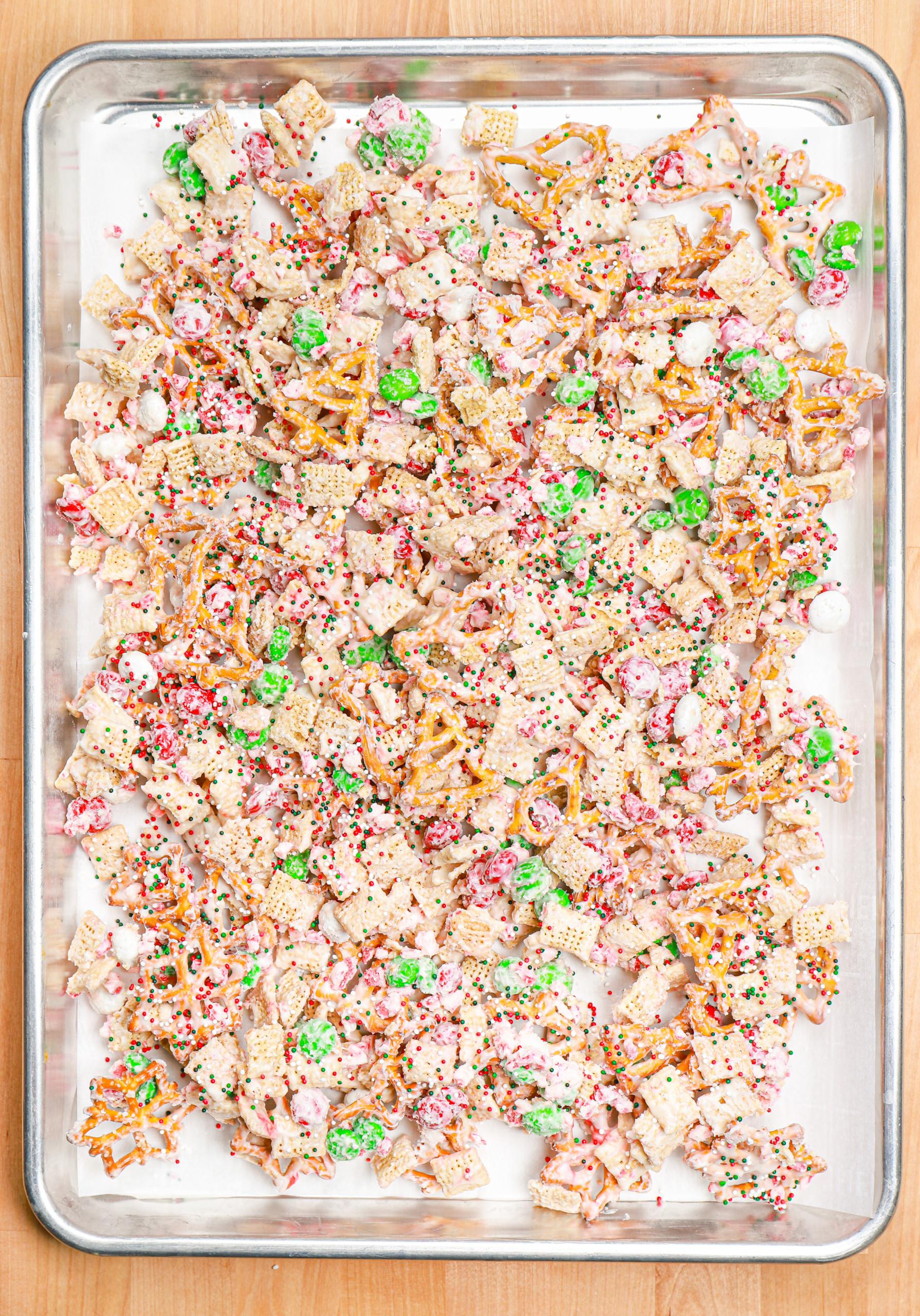 Peppermint crunch snack mix spread out on a parchment paper lined baking sheet.