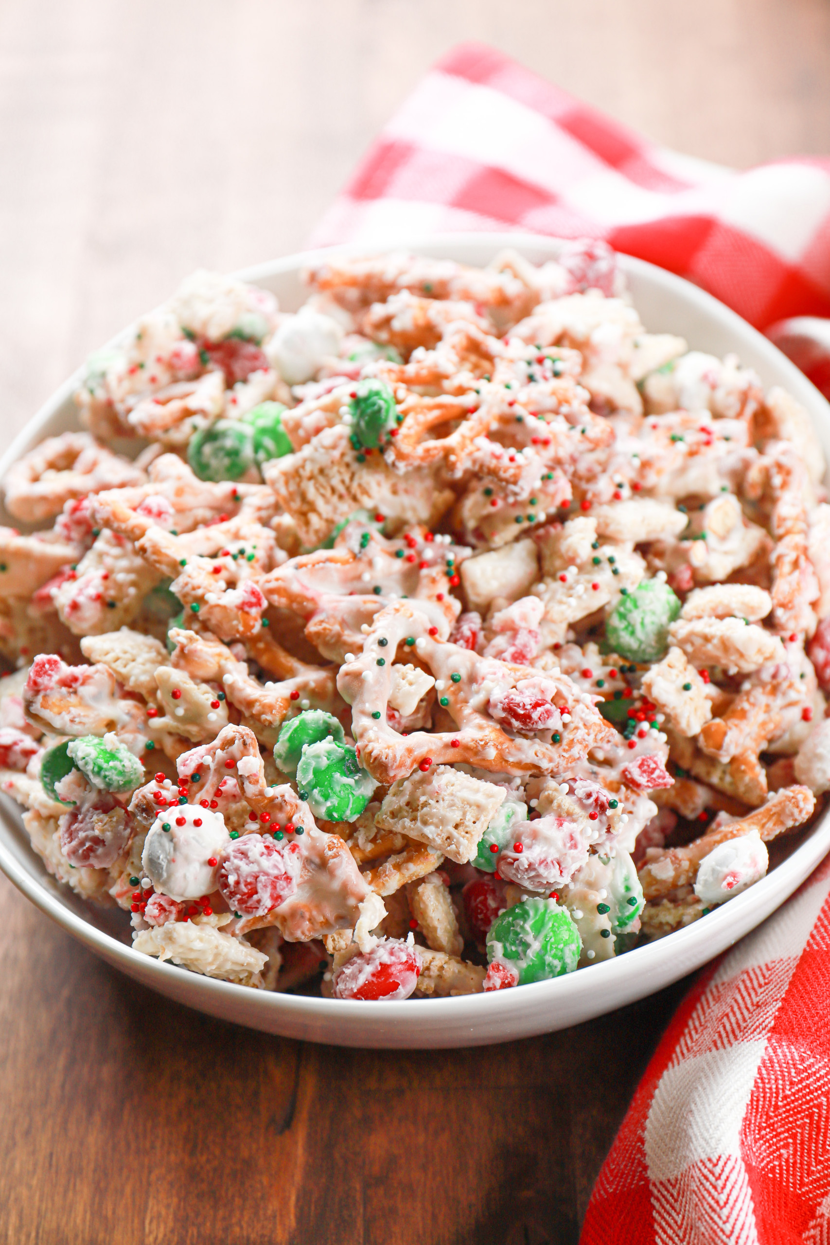 Peppermint crunch chex mix in a large white bowl alongside a red checked towel.