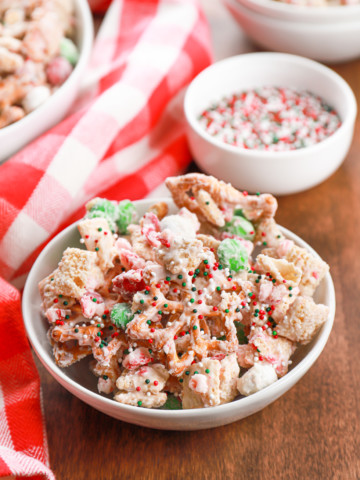 Small white bowl full of peppermint crunch snack mix on a wooden board.