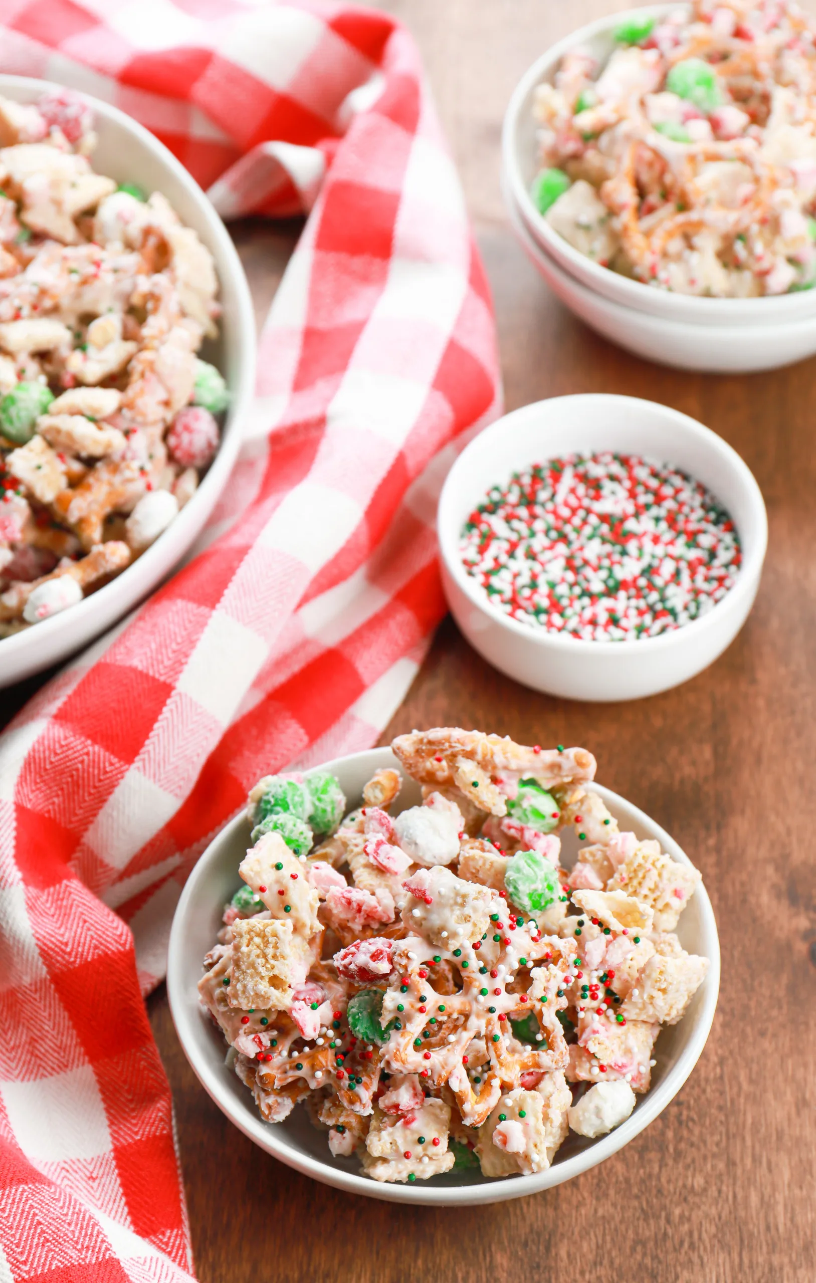 Overhead view of three white bowls full of peppermint crunch snack mix on a wooden board.