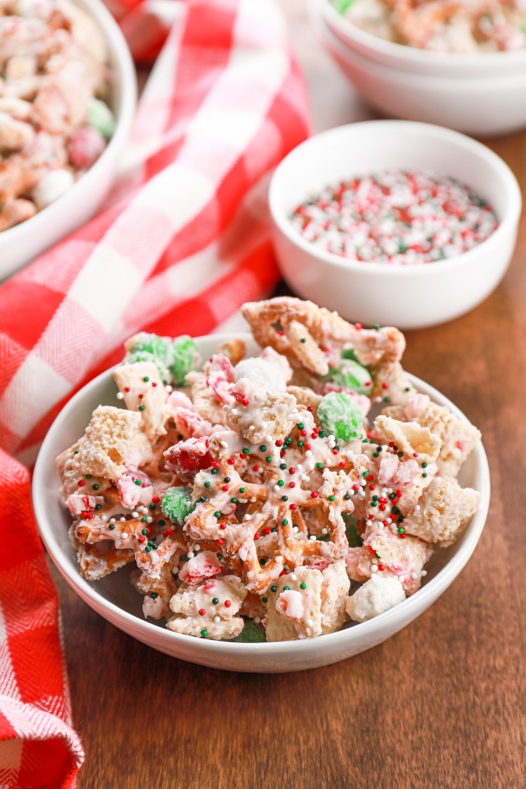 Small white bowl full of peppermint crunch snack mix on a wooden board.