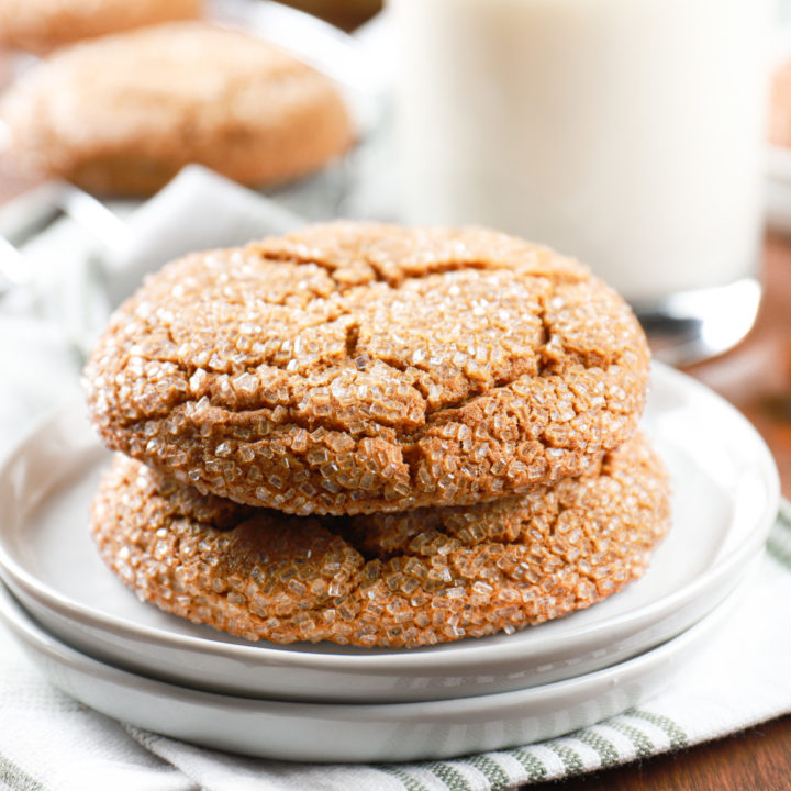 Two chewy molasses cookies stacked on a small white plate with a glass of milk in the background.