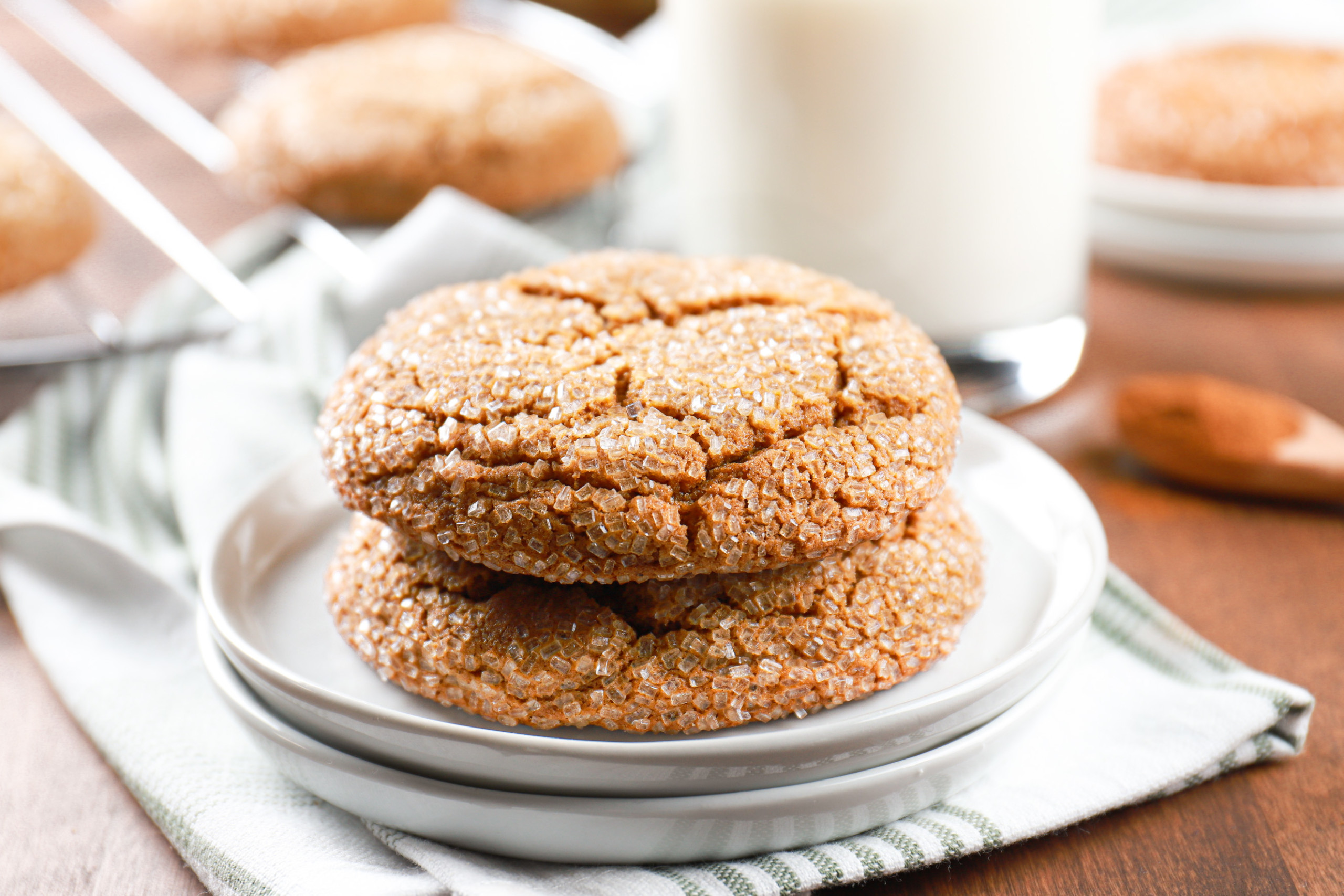Two chewy molasses cookies stacked on a small white plate with a glass of milk in the background.