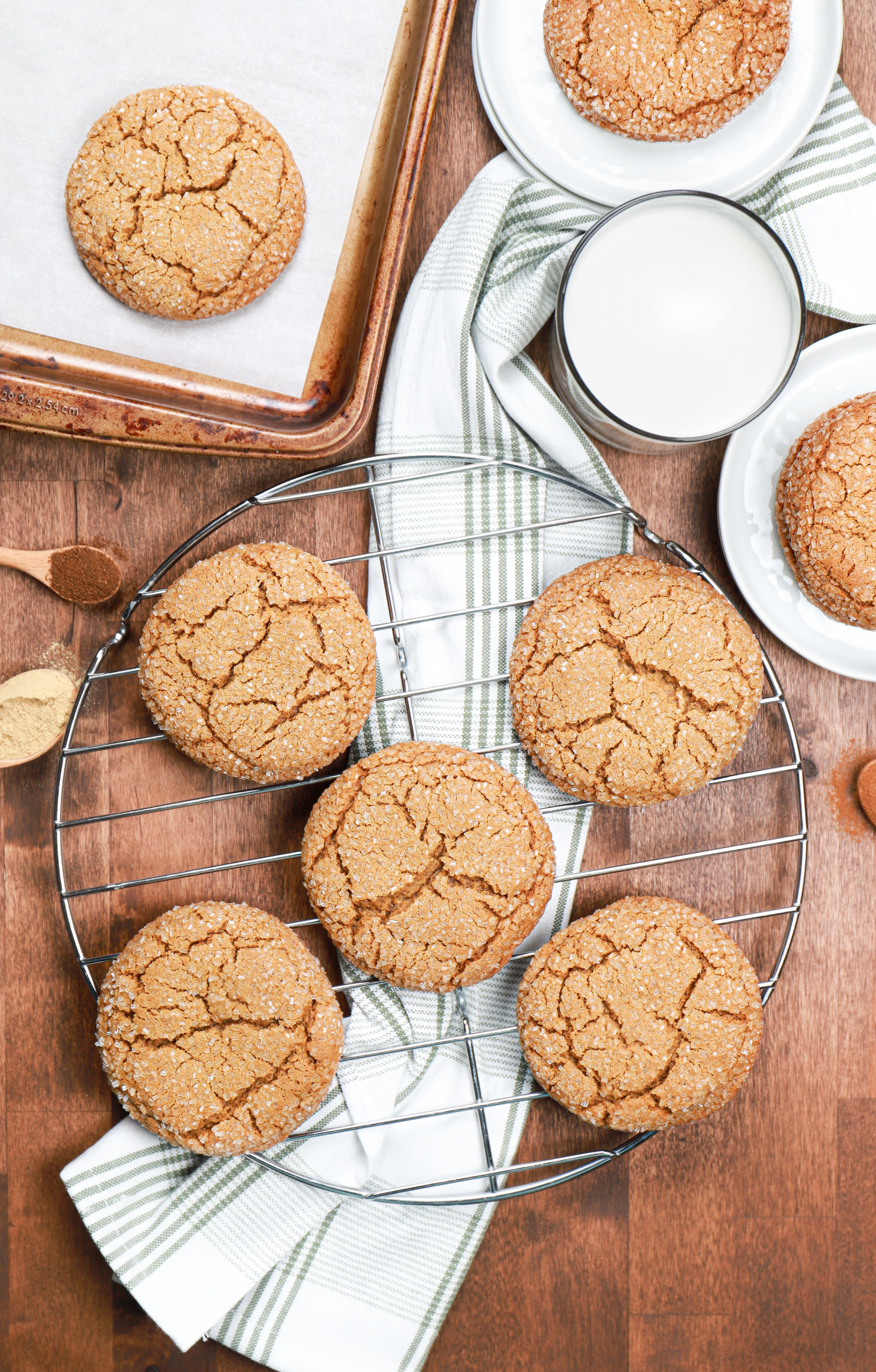 Overhead view of bakery style molasses cookies on a cooling rack over a green and white dish towel.