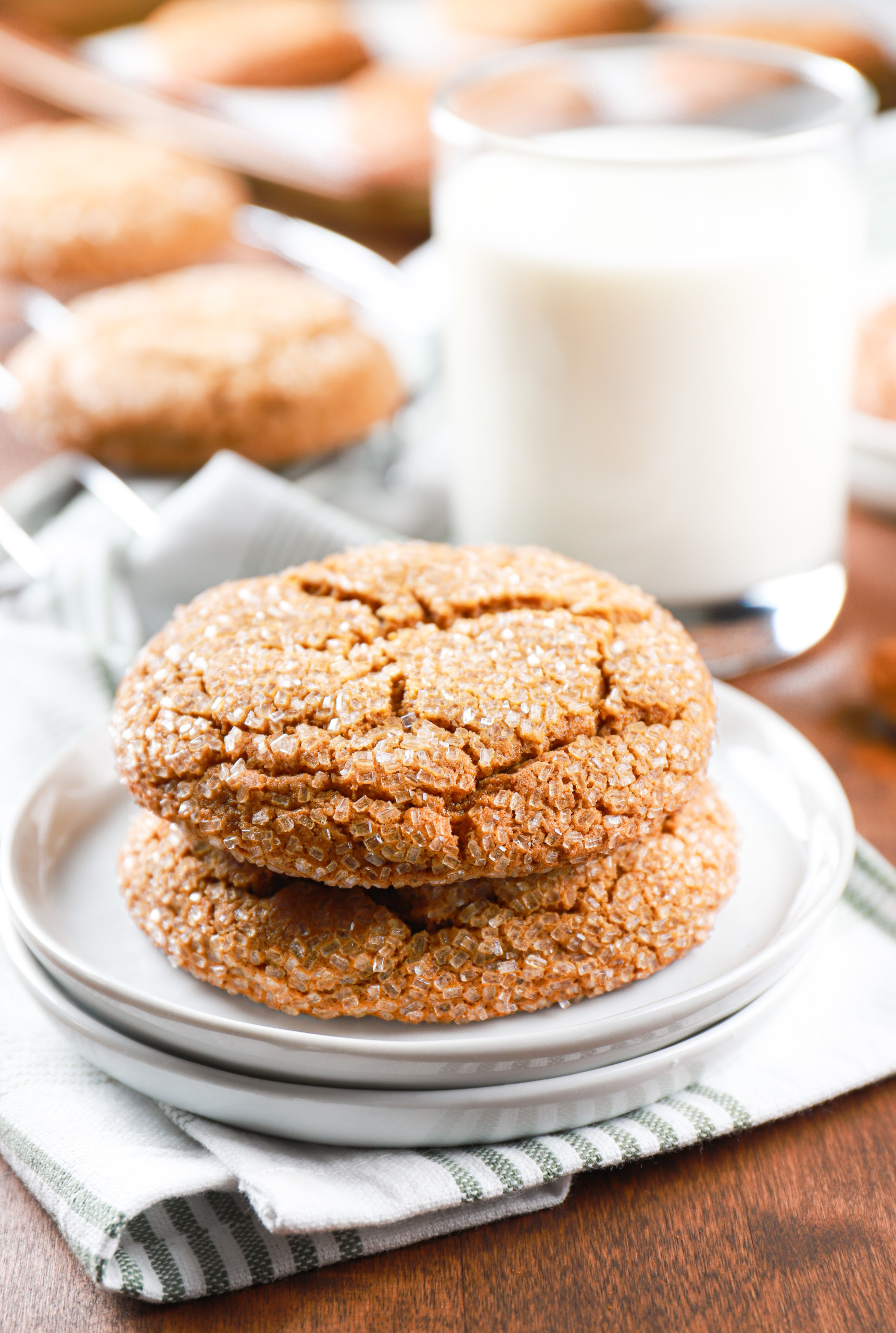 Two ginger molasses cookies stacked on a small white plate with a cooling rack of cookies in the background.