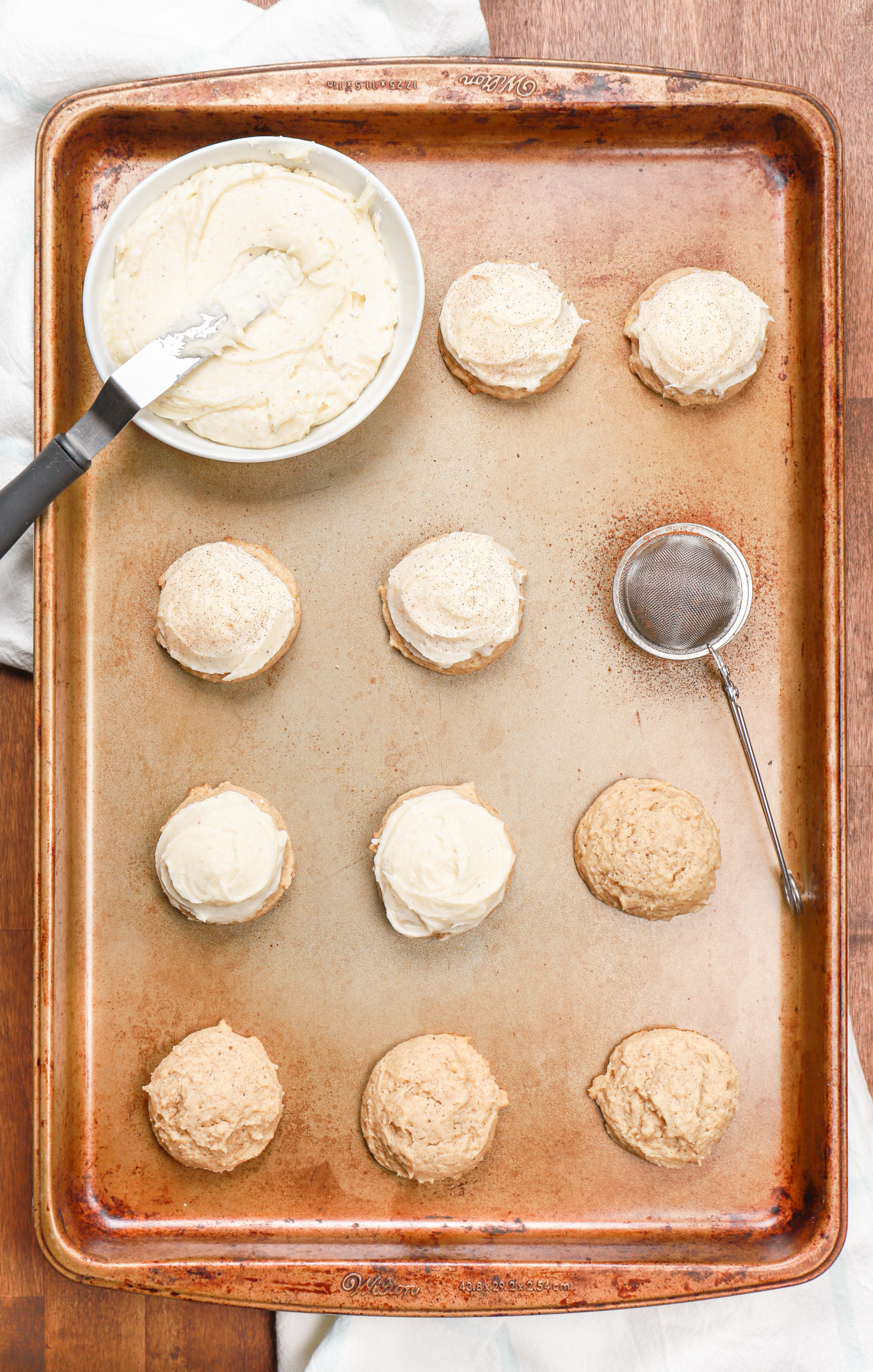 Overhead view of a batch of eggnog cookies being frosted and sprinkled with nutmeg.