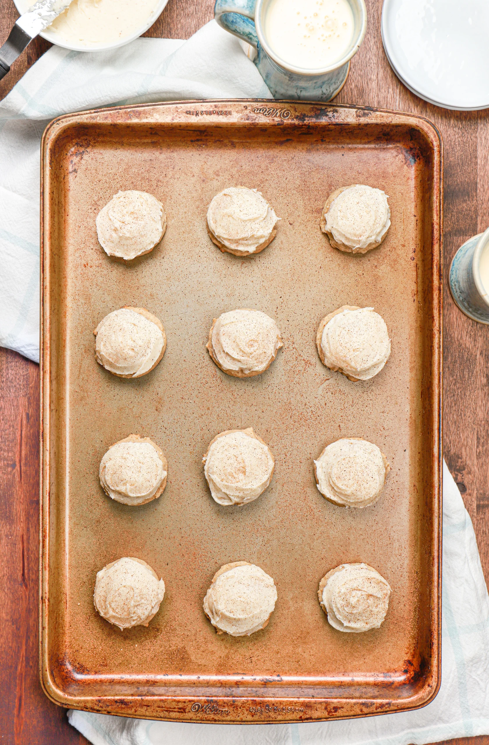 Overhead view of a batch of frosted eggnog cookies on a baking sheet.