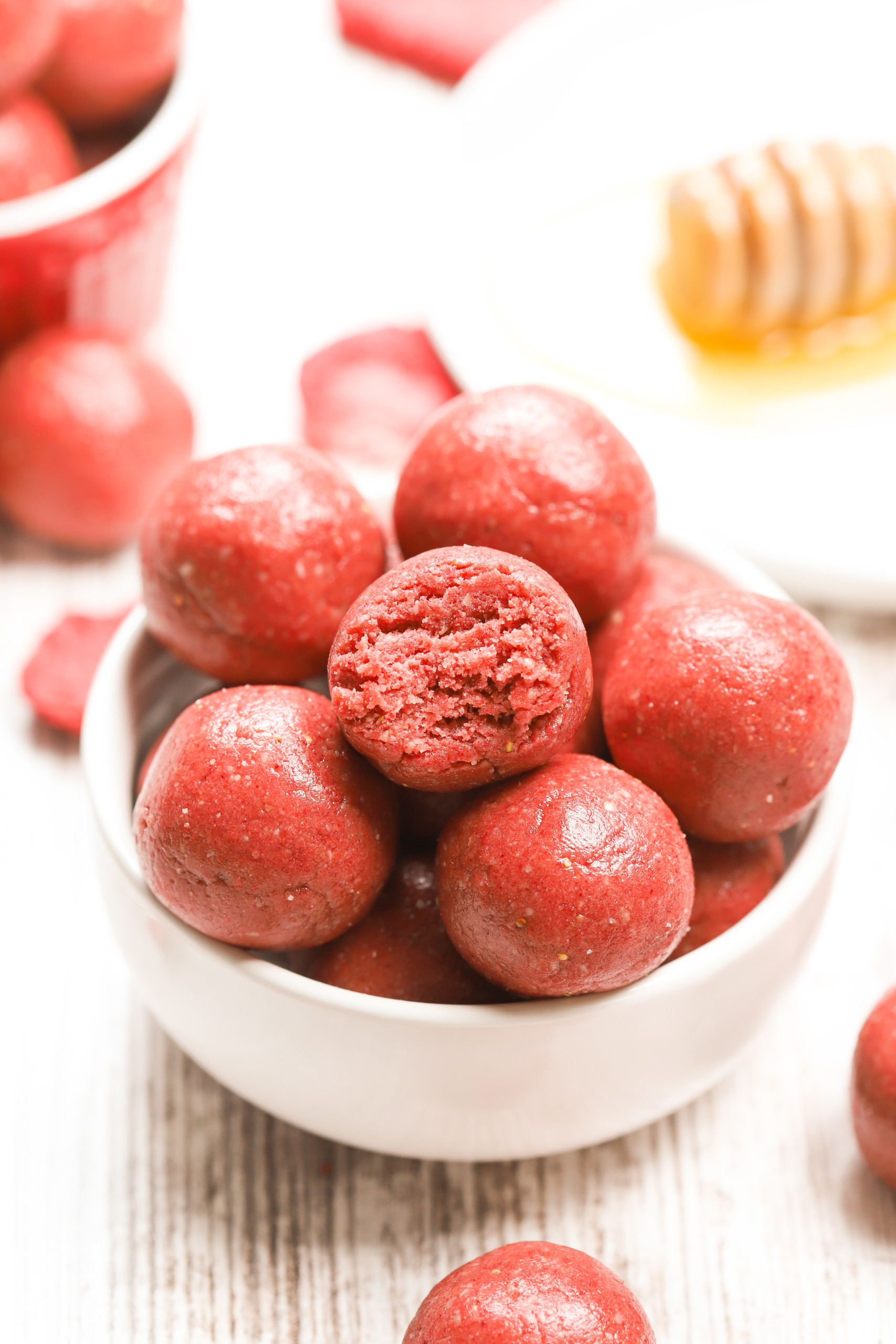 Up close side view of a strawberry vanilla protein bite with a bite taken out of it in a small white bowl full of protein bites.