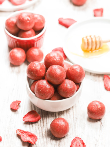 A small white bowl full of strawberry vanilla protein bites with a small red bowl full of bites in the background.