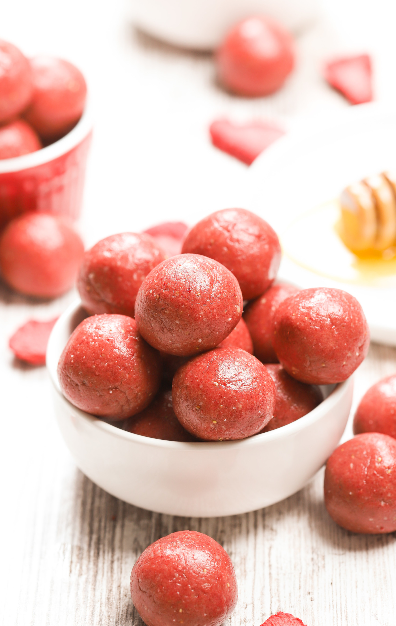 Side view of a small white bowl full of strawberry vanilla energy bites with more bites in the background and freeze-dried strawberries scattered around.