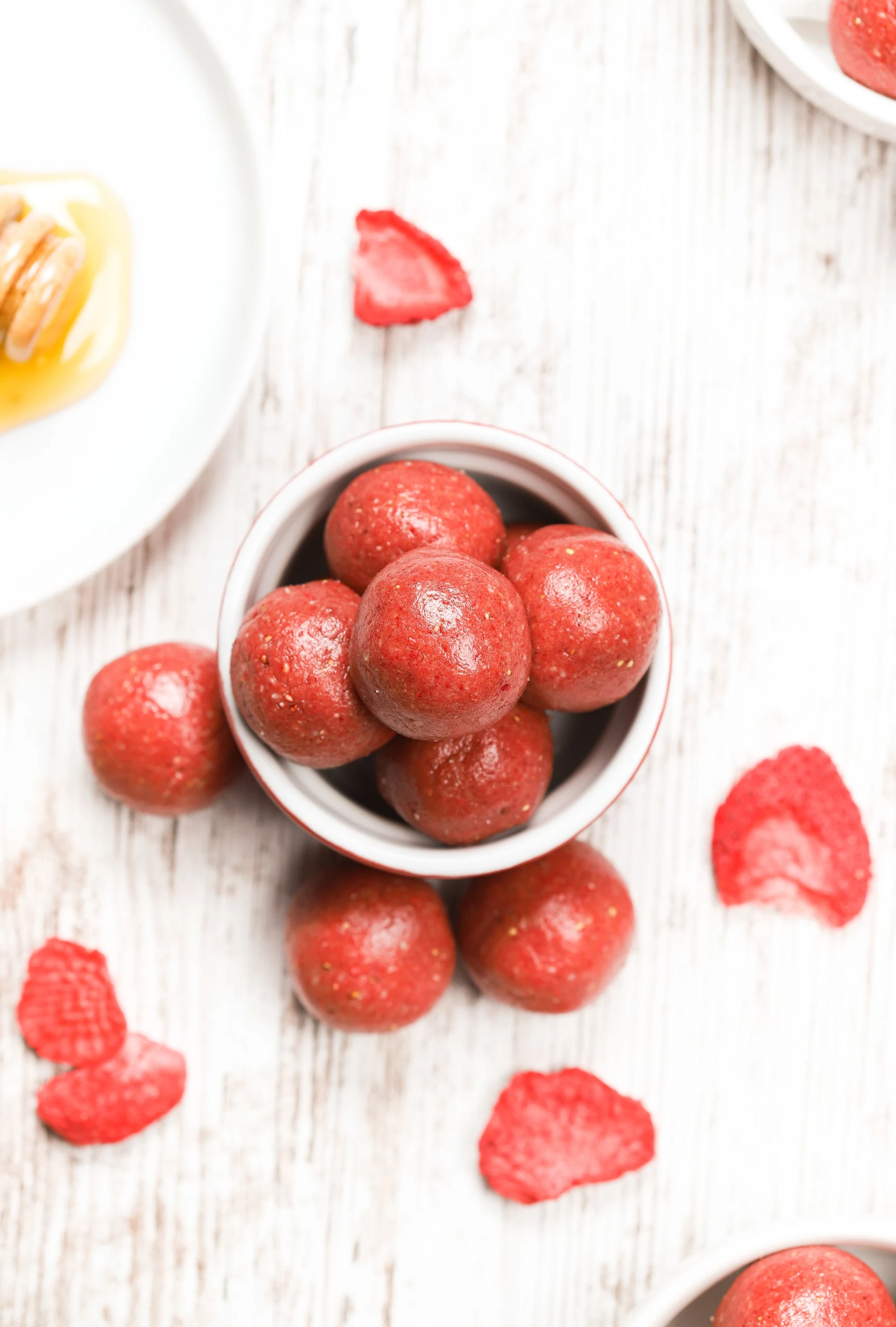 Overhead view of a small red bowl full of strawberry vanilla protein balls.