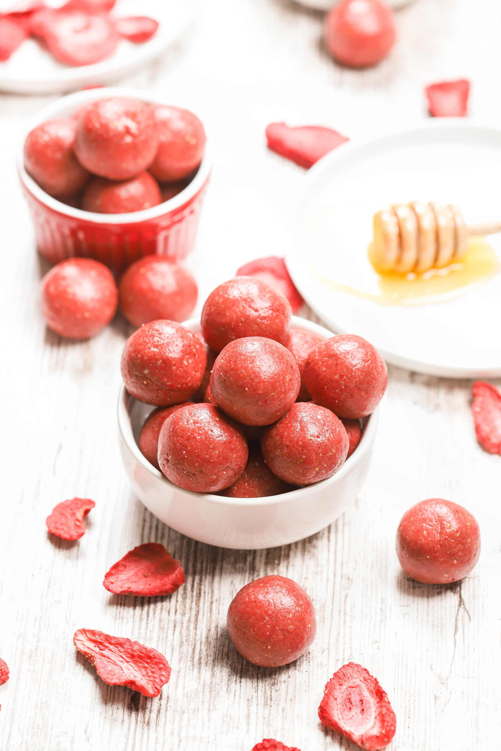 A small white bowl full of strawberry vanilla protein bites with a small red bowl full of bites in the background.