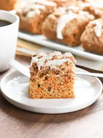 Up close side view of a piece of carrot coffee cake on a small white plate with the remaining cake on a blue plate in the background.