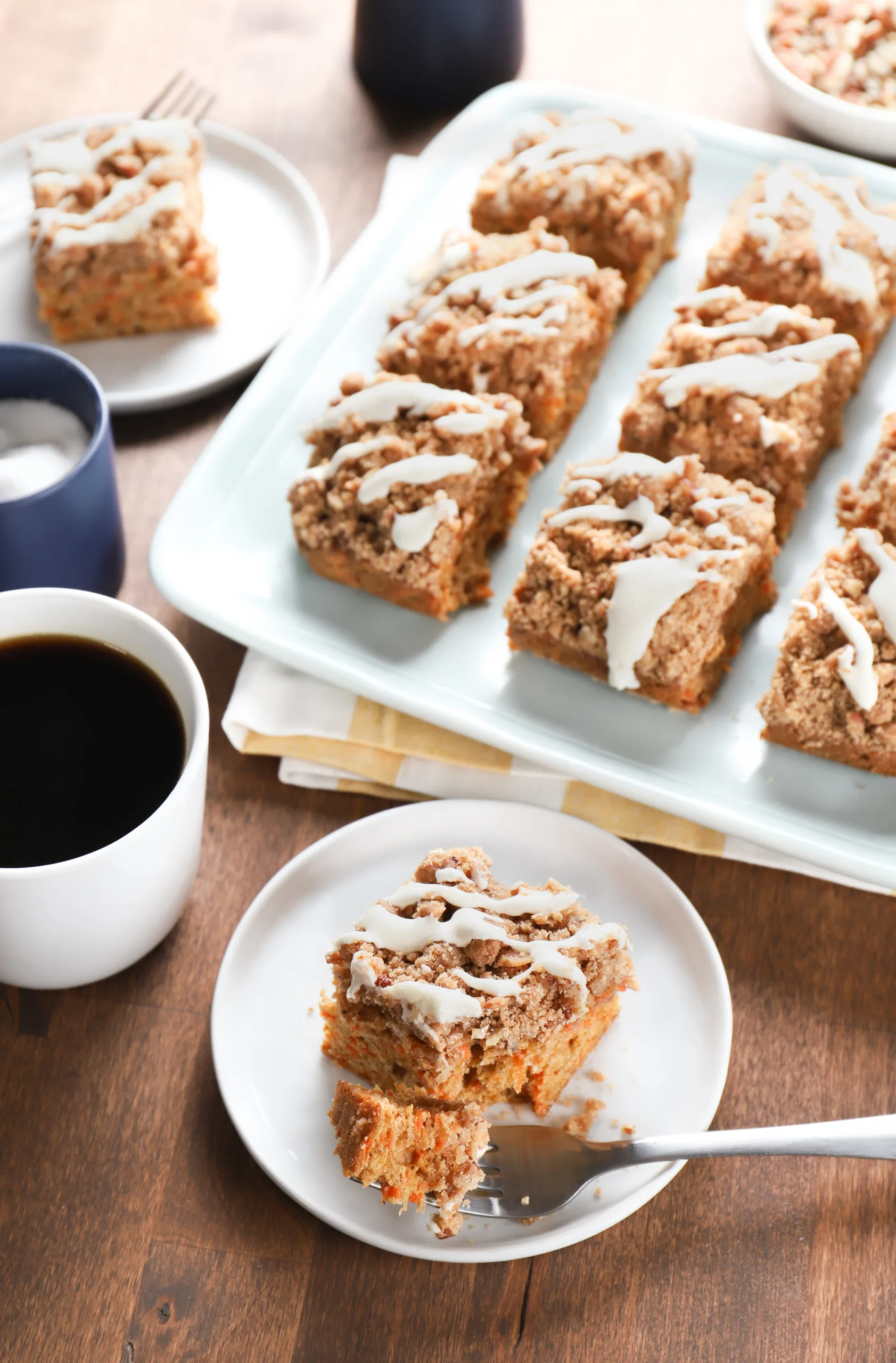 Overhead view of a piece of carrot cake coffee cake on a small white plate with the remainder of the cake on a blue plate in the background.