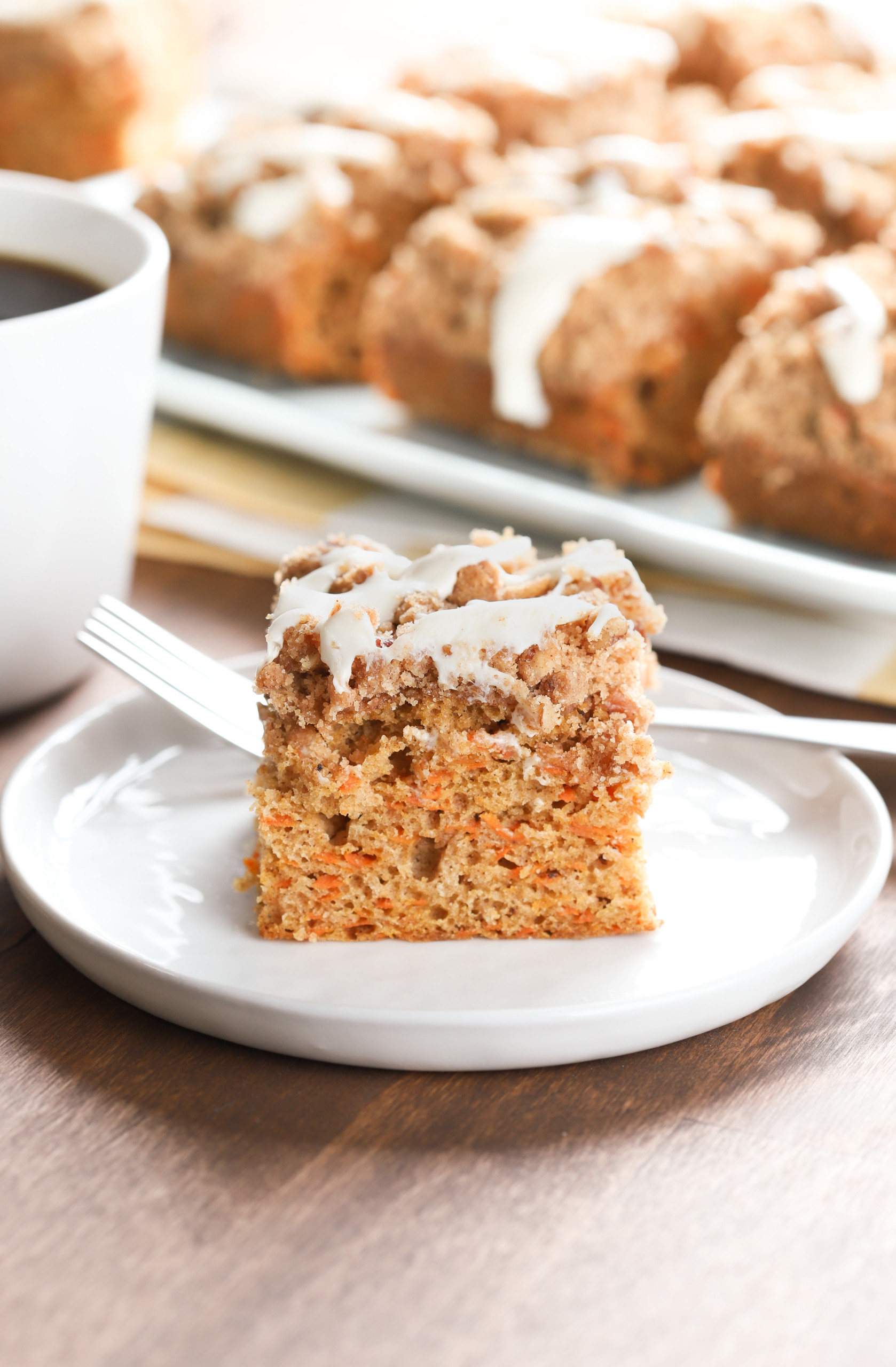 Up close side view of a piece of carrot coffee cake on a small white plate with the remaining cake on a blue plate in the background.
