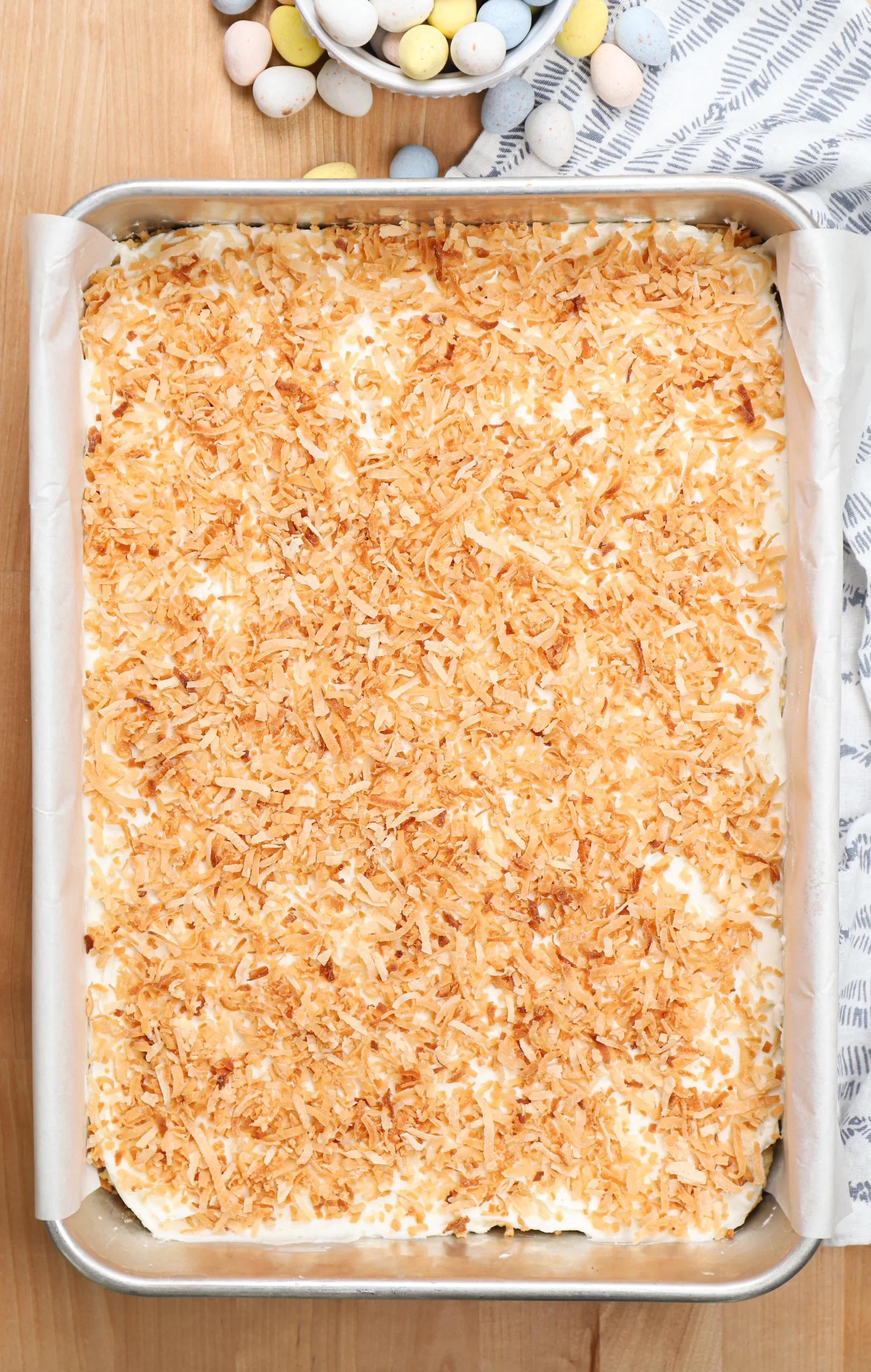 Overhead view of a batch of frosted coconut sugar cookie bars in an aluminum baking dish.