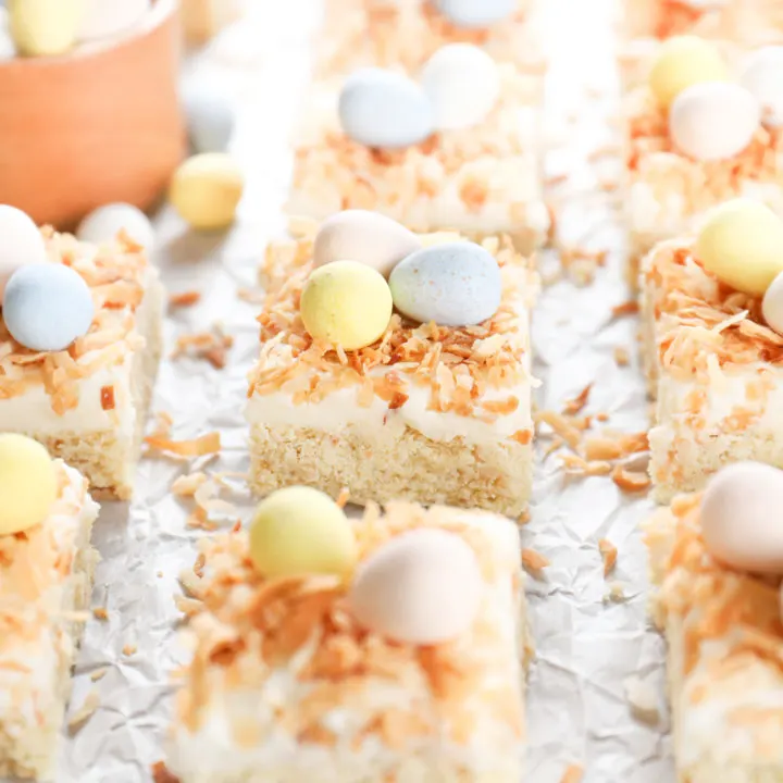 A side view of a batch of frosted coconut cookie bars on a piece of white parchment paper.