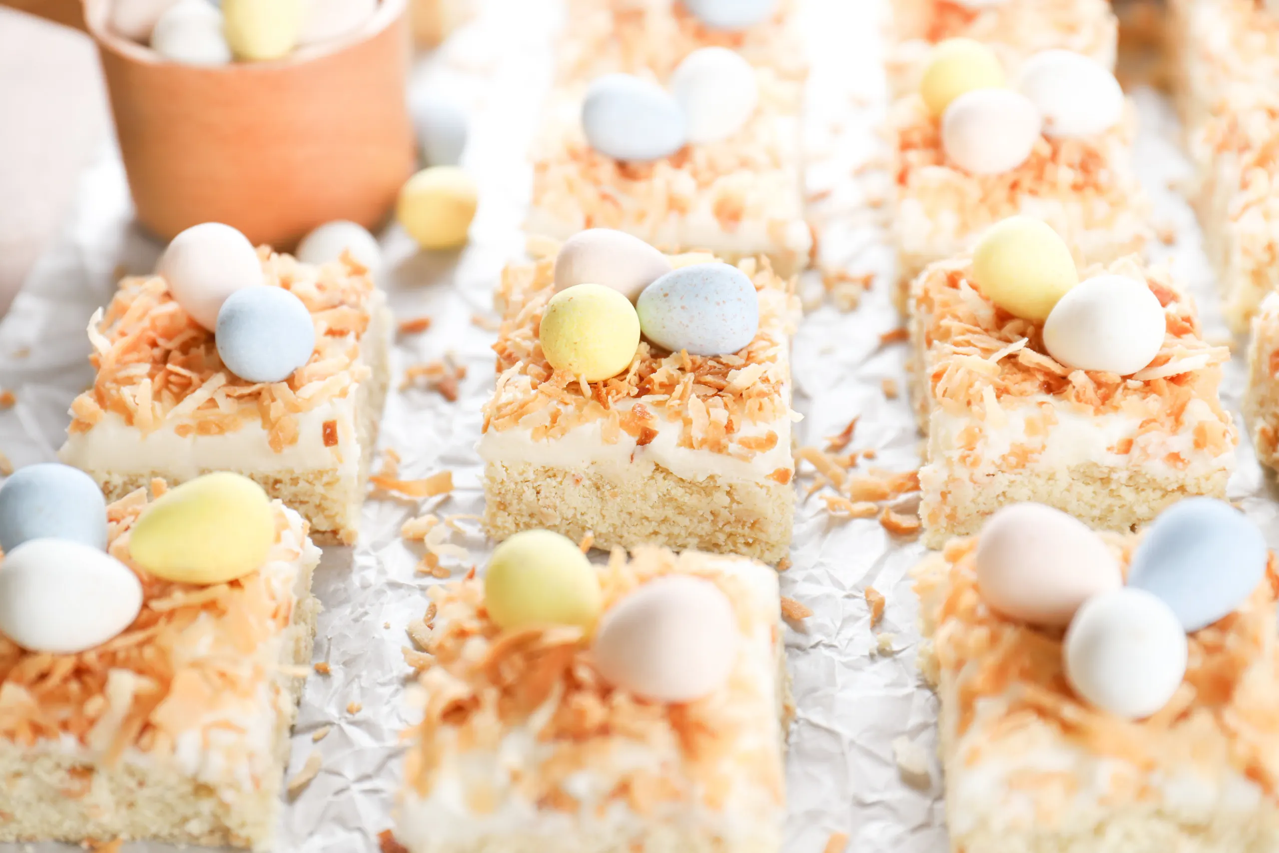 A side view of a batch of frosted coconut cookie bars on a piece of white parchment paper.