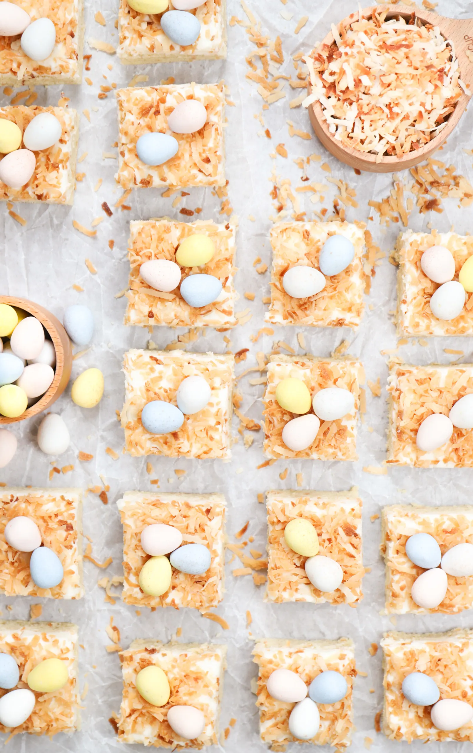 Overhead view of a batch of frosted coconut sugar cookie bars cut into pieces on a piece of parchment paper.