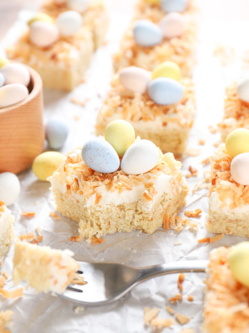 A frosted coconut sugar cookie bar on a piece of parchment paper with a bite taken out of it.