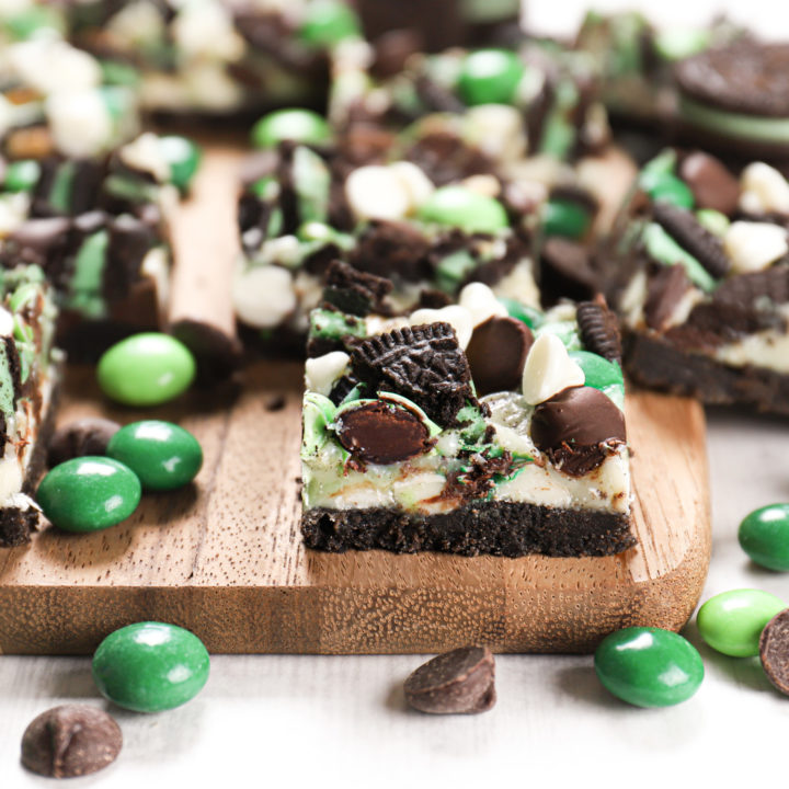 Side view of a mint chocolate seven layer bar on a wooden cutting board with more bars in the background.