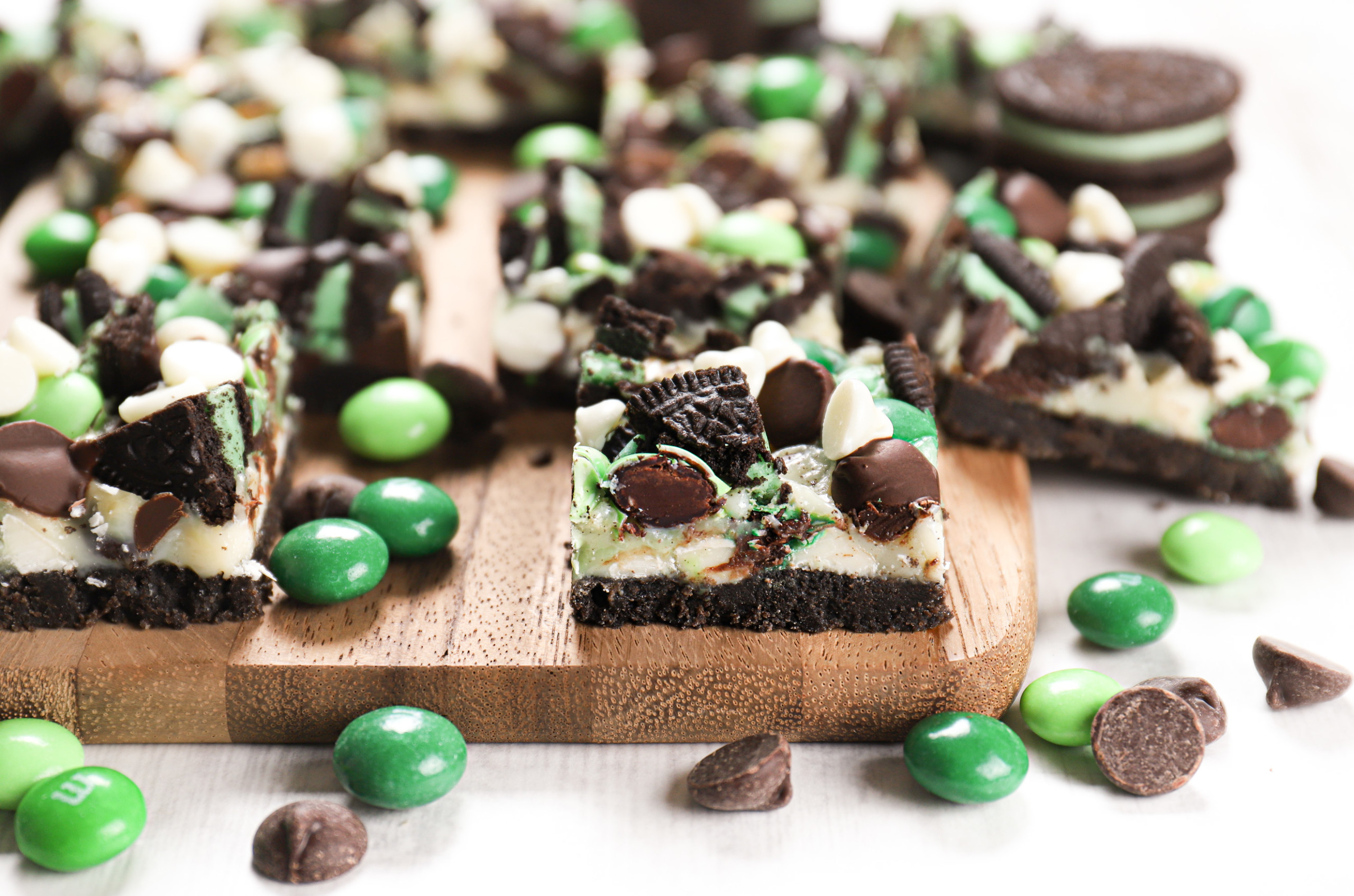 Side view of a mint chocolate seven layer bar on a wooden cutting board with more bars in the background.