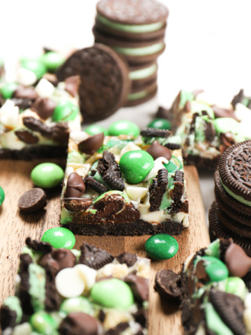 Up close side view of a mint chocolate seven layer bar surrounded by additional bars on a wooden cutting board.