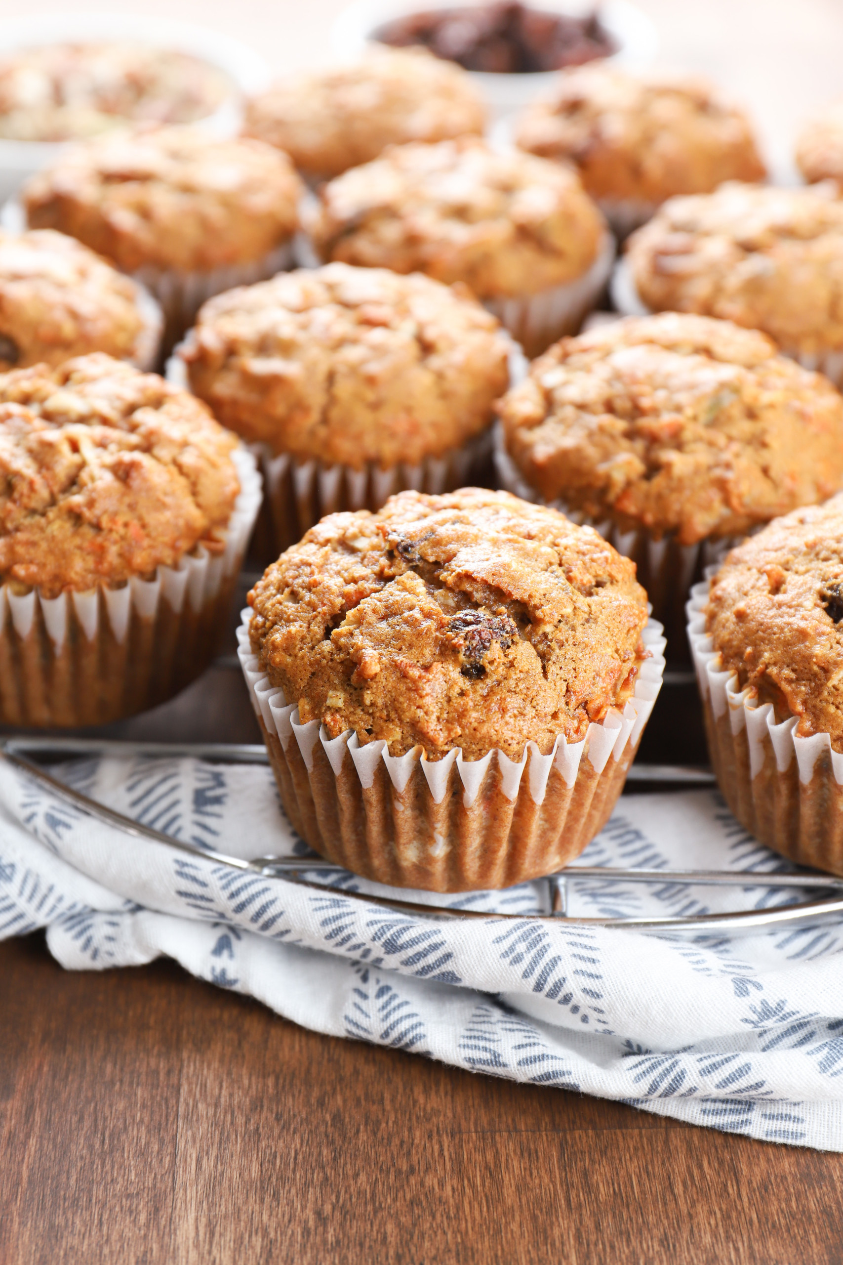 Side view of a batch of morning glory muffins on a cooling rack on top of a blue and white towel.