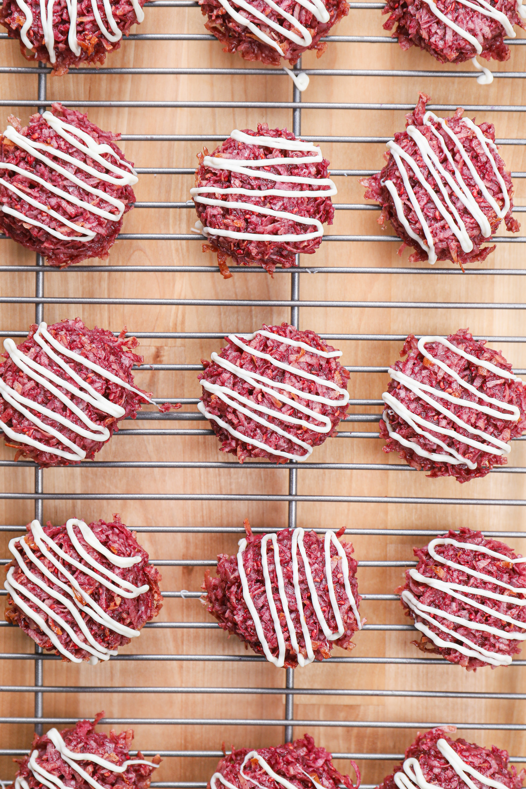 Up close overhead view of a batch of raspberry coconut macaroons drizzled with white chocolate.