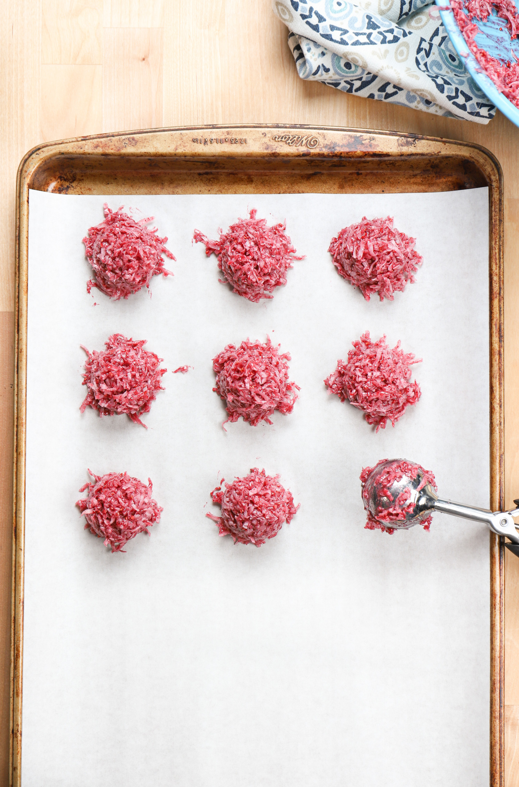 Overhead view of raspberry coconut macaroons being scooped onto a baking sheet with a cookie scoop.