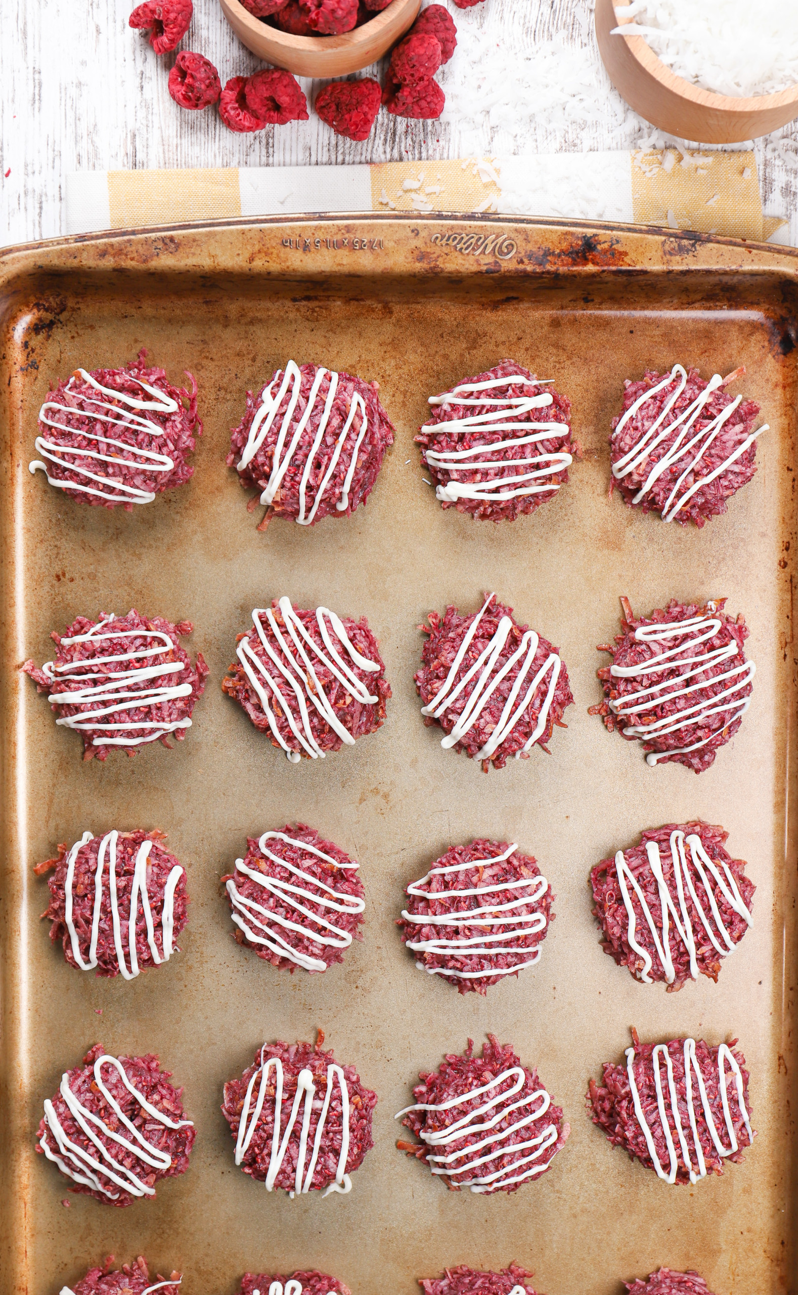 Overhead view of a batch of raspberry coconut macaroons on an aluminum baking sheet.
