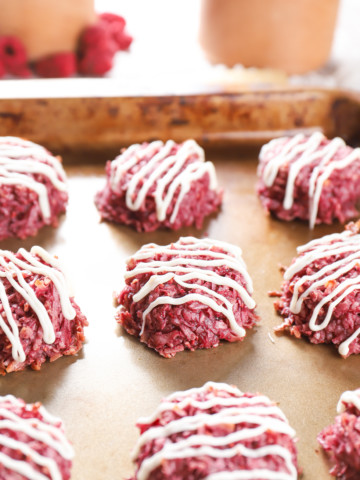 Side view of a raspberry coconut macaroon on an aluminum baking sheet surrounded by the remaining batch of macaroons.