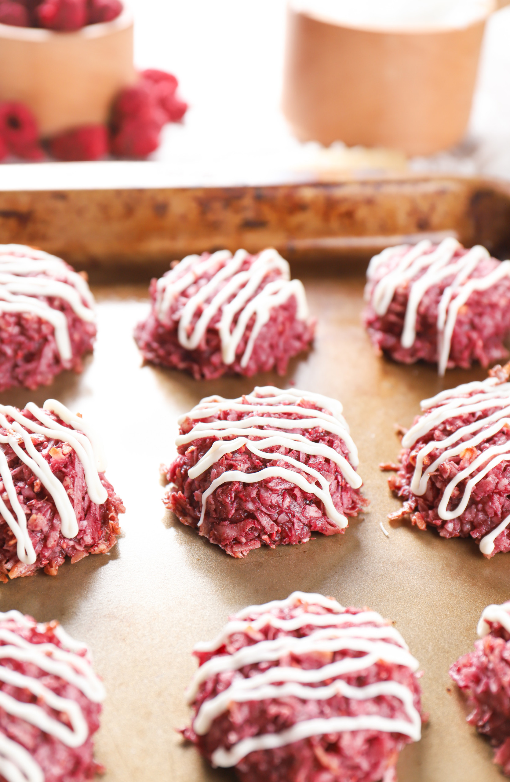 Side view of a raspberry coconut macaroon on an aluminum baking sheet surrounded by the remaining batch of macaroons.