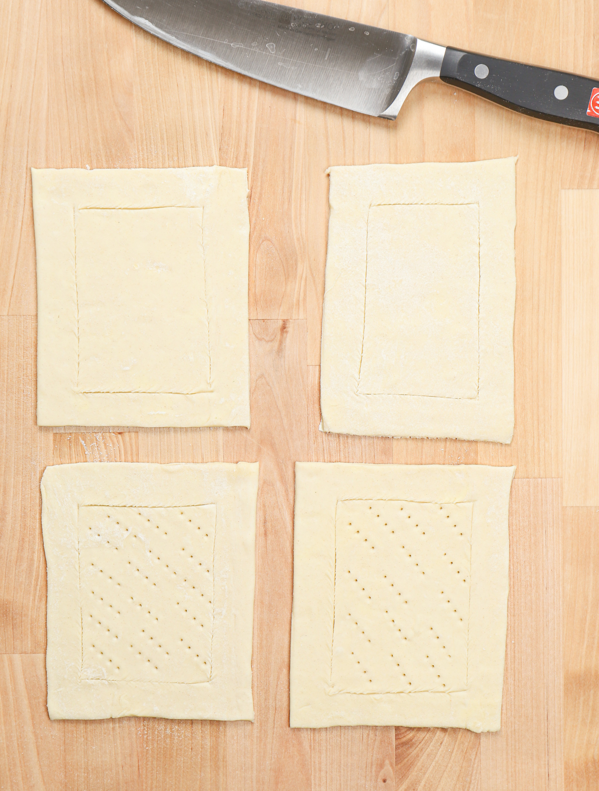 Four pieces of puff pastry scored along the edges on a wooden countertop.