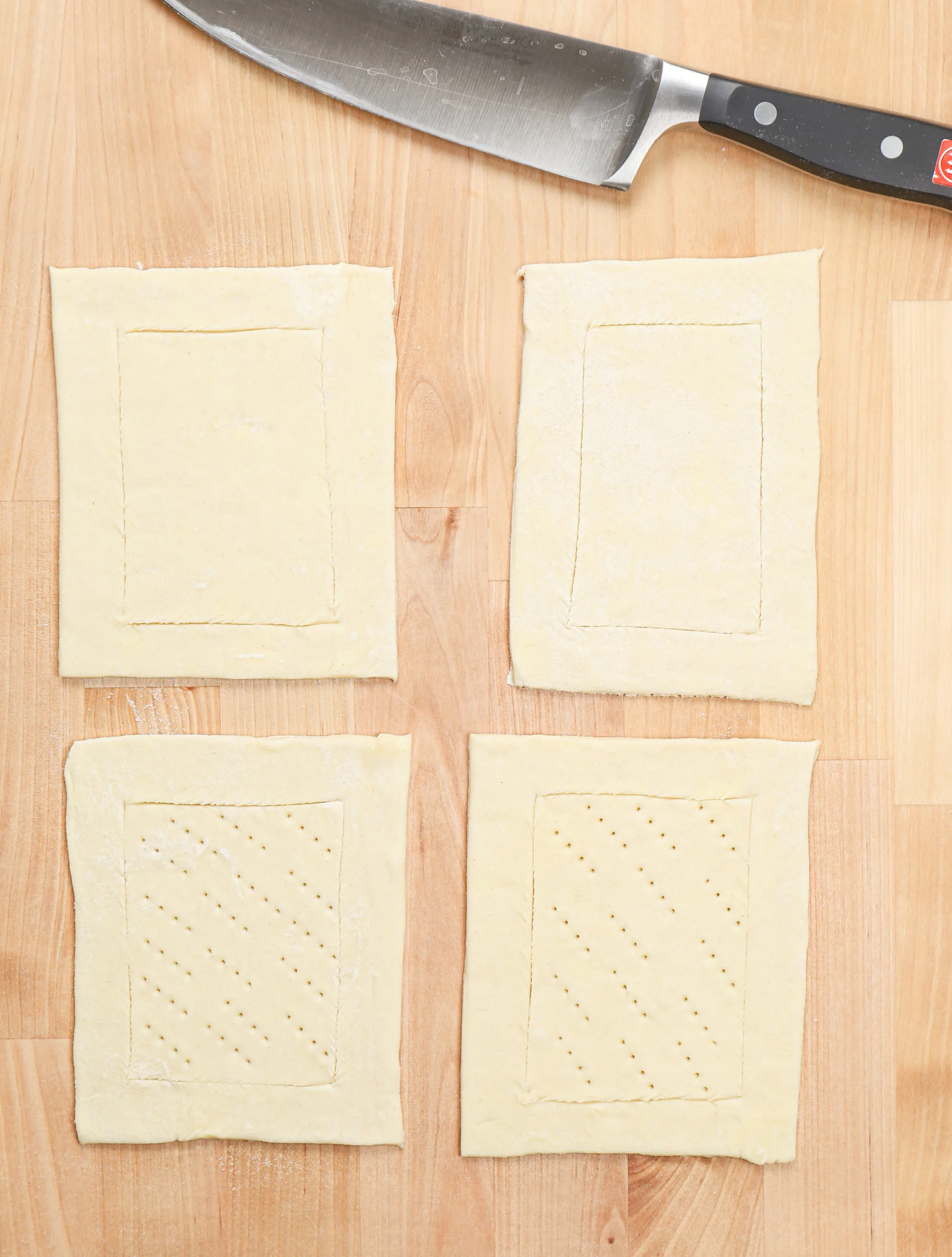 Four pieces of puff pastry scored along the edges on a wooden countertop.