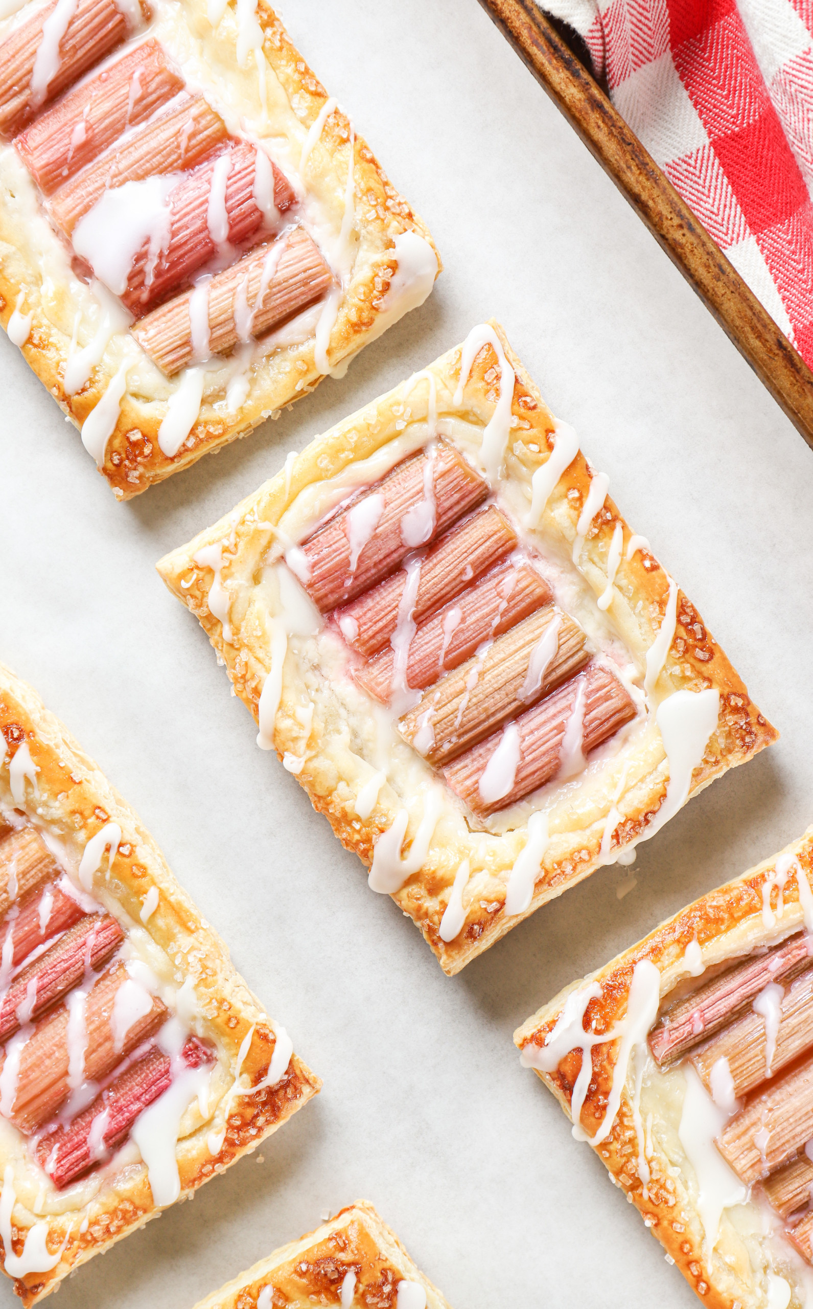 Up close overhead view of a rhubarb cream cheese danish drizzled with a glaze on a parchment paper lined baking sheet.