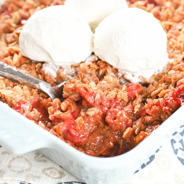 Up close view of a scoop of strawberry rhubarb crisp in a light blue baking dish.