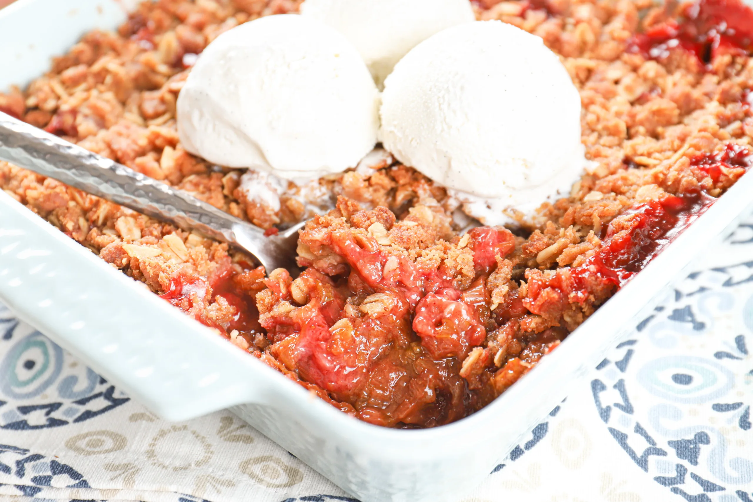 Up close view of a scoop of strawberry rhubarb crisp in a light blue baking dish.