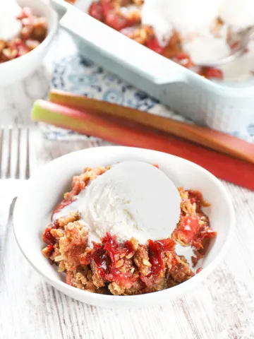 Strawberry rhubarb crisp in a small white bowl topped with a scoop of vanilla ice cream.