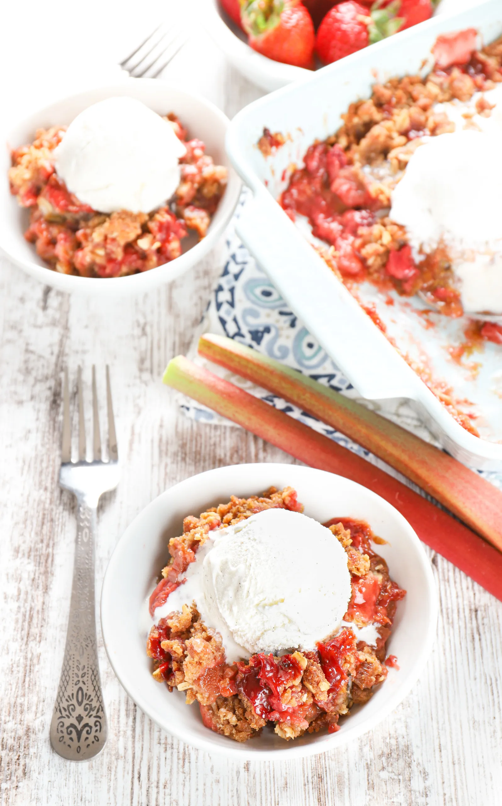 Overhead view of two small white bowls filled with strawberry rhubarb crisp and topped with a scoop of vanilla ice cream.