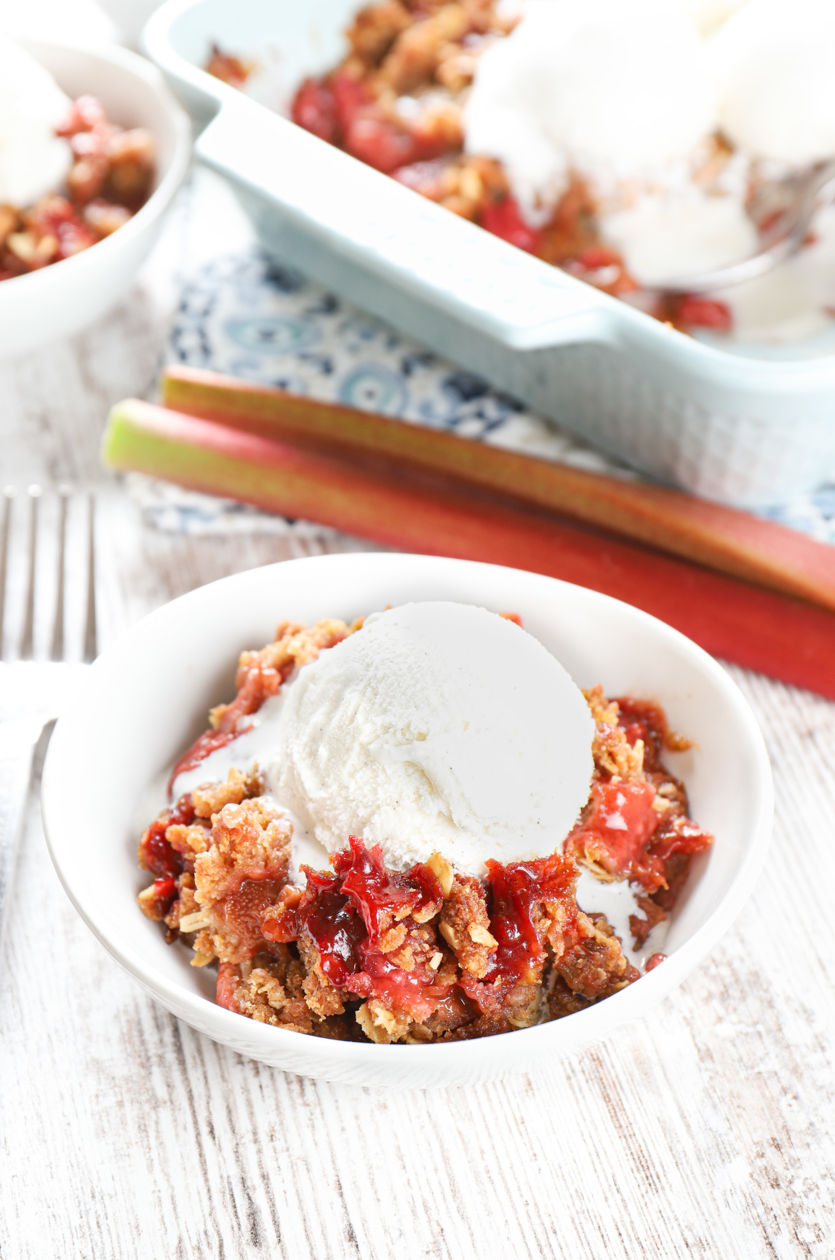 Strawberry rhubarb crisp in a small white bowl topped with a scoop of vanilla ice cream.