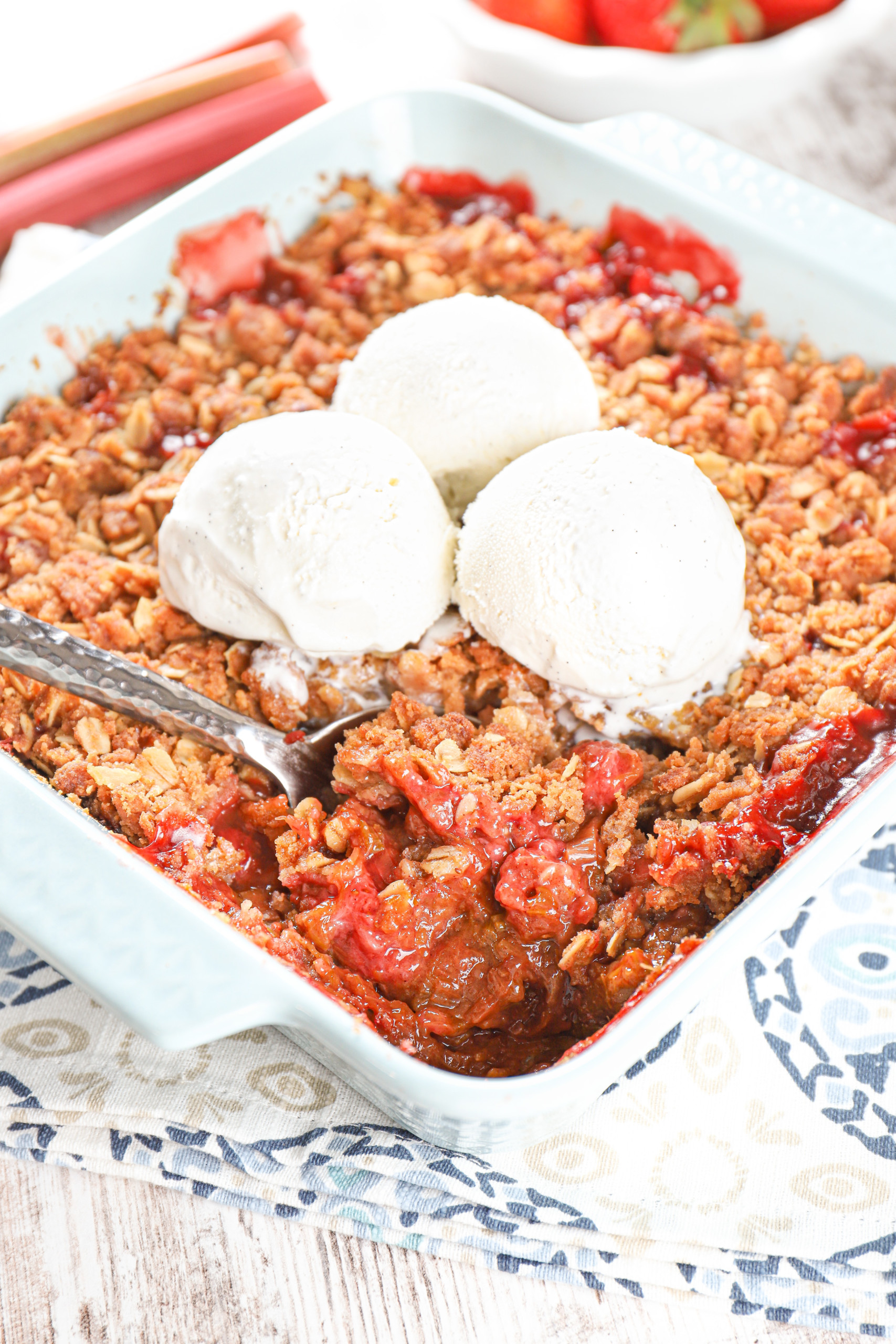 Overhead view of a scoop of strawberry rhubarb crisp in a light blue baking dish.