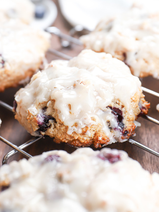 Up close side view of a baked blueberry fritter on a cooling rack surrounded by other fritters.